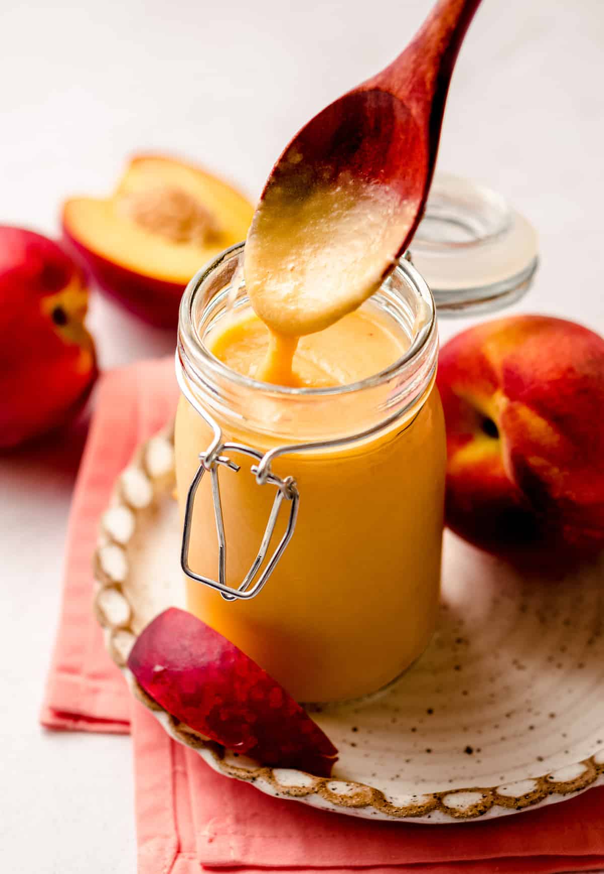 a spoon pulling a scoop of peach curd out of a jar