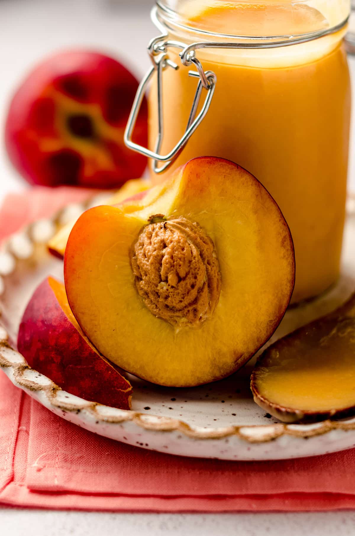 a peach sliced in half with a jar of peach curd in the background