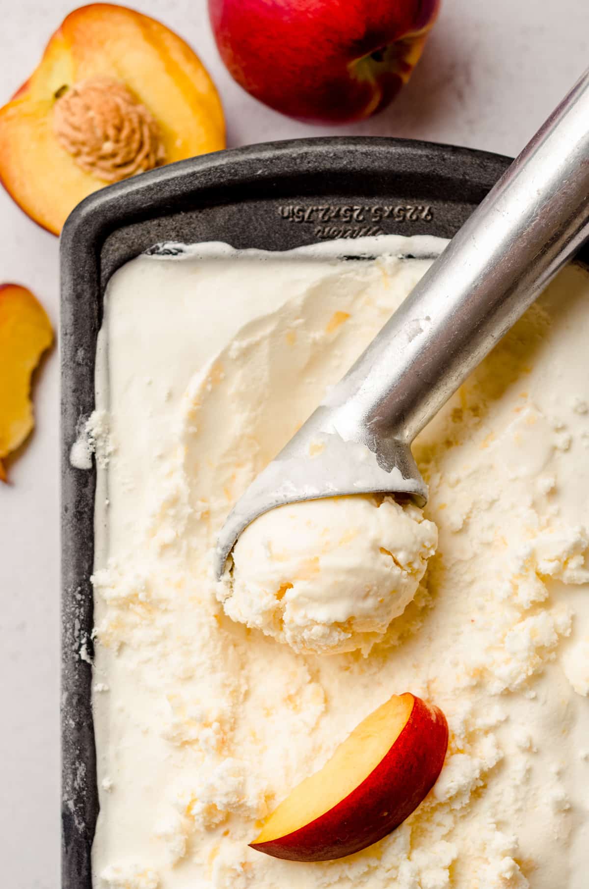 ice cream scooper in a container of homemade peach ice cream