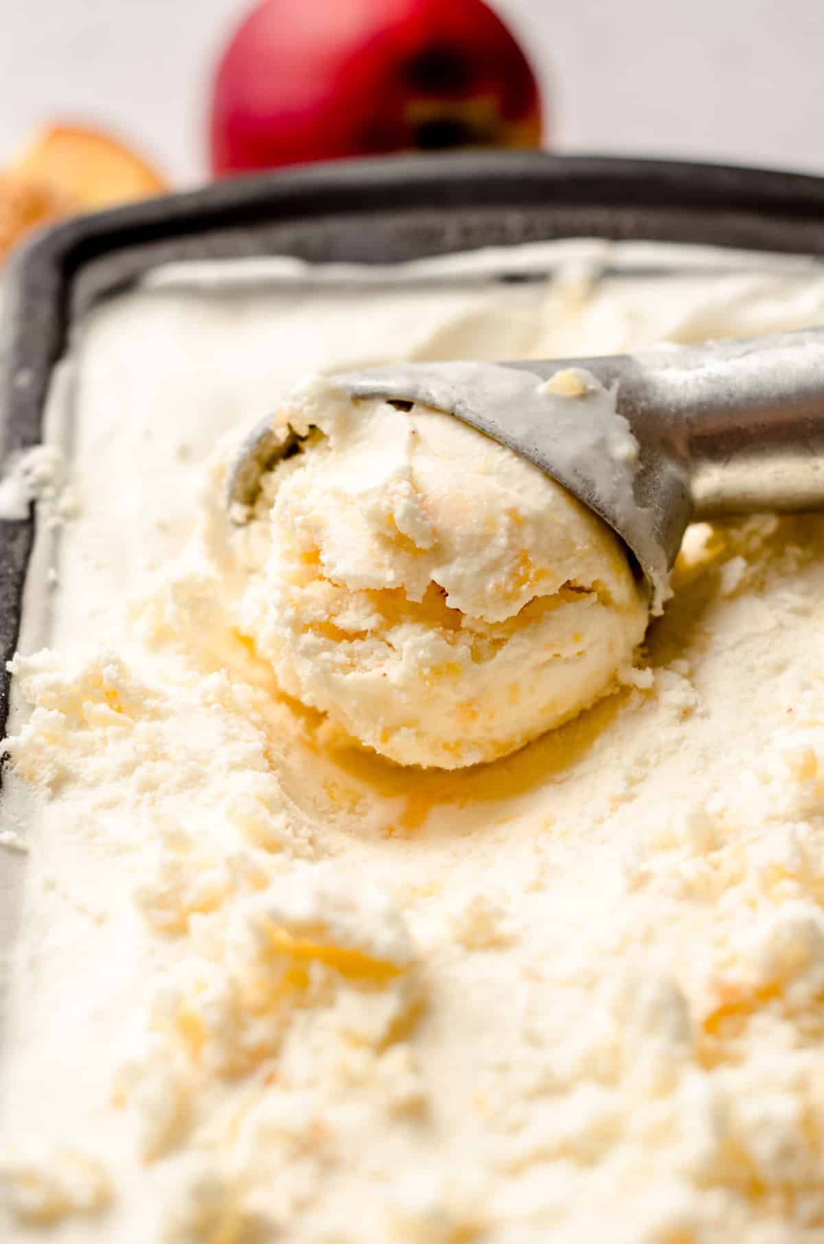 ice cream scooper in a container of homemade peach ice cream