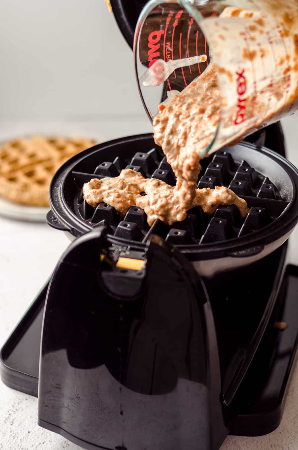 pouring carrot cake waffle batter into a waffle iron