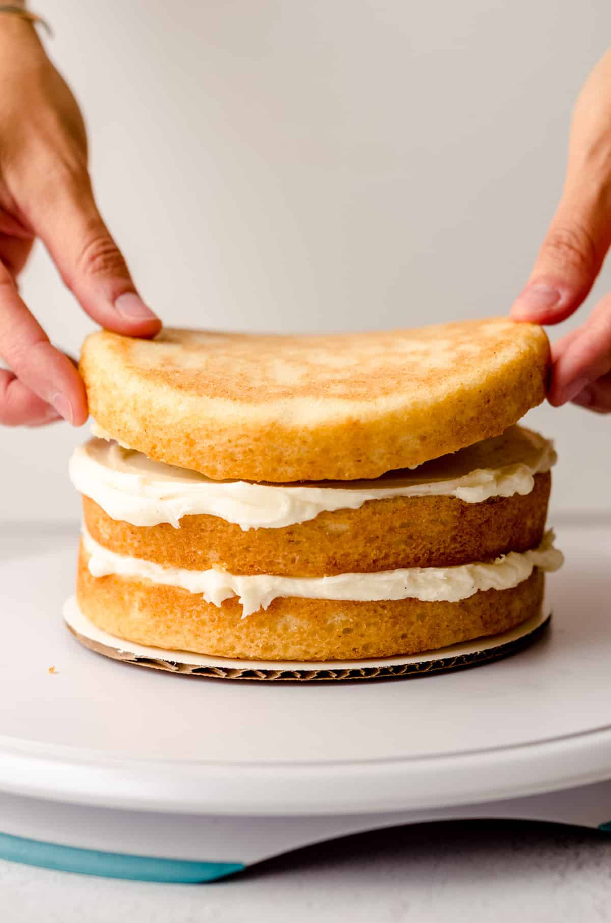 hands putting a third layer on a stacked cake