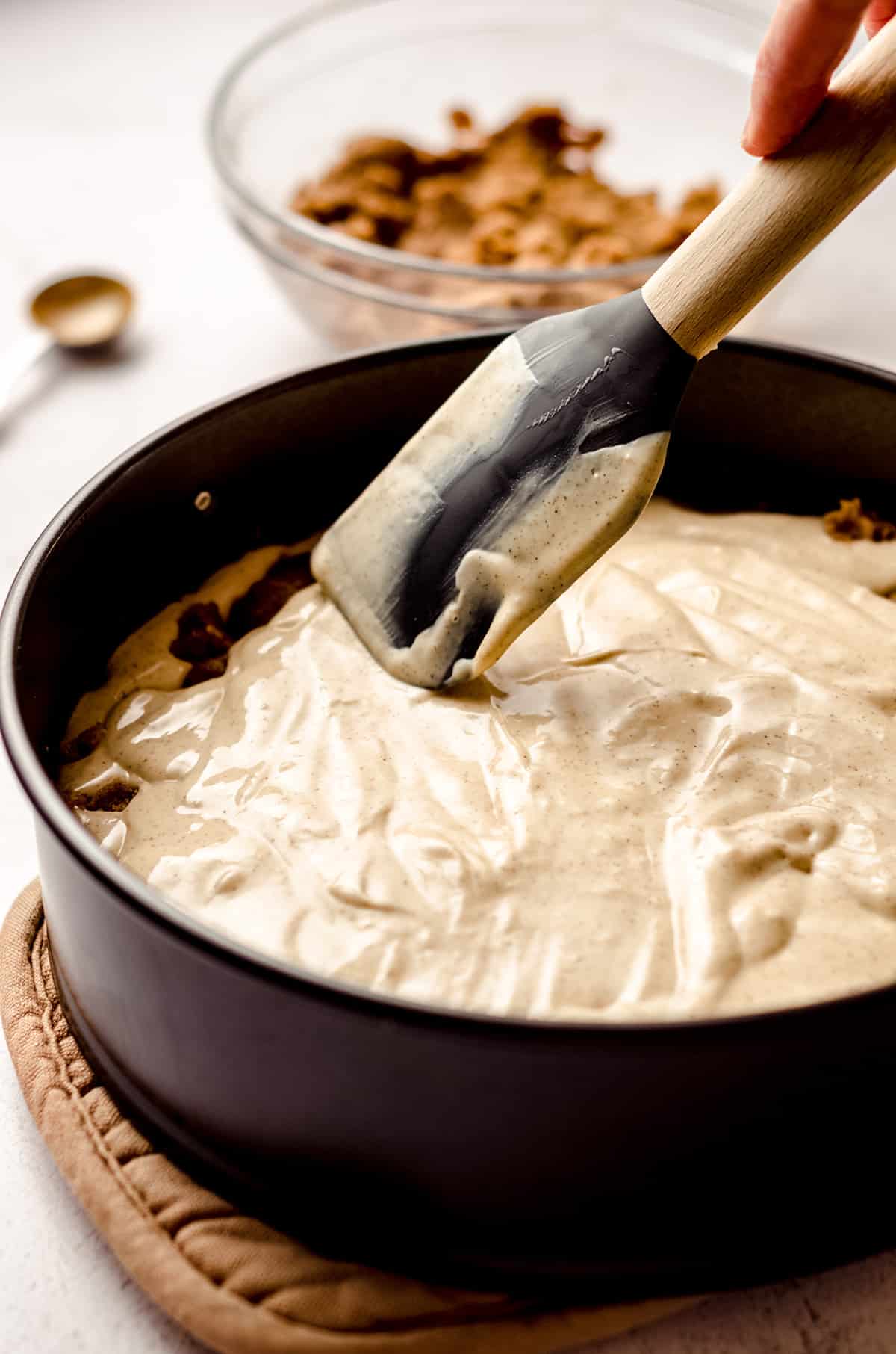 spatula spreading cinnamon roll cheesecake batter onto a springform pan