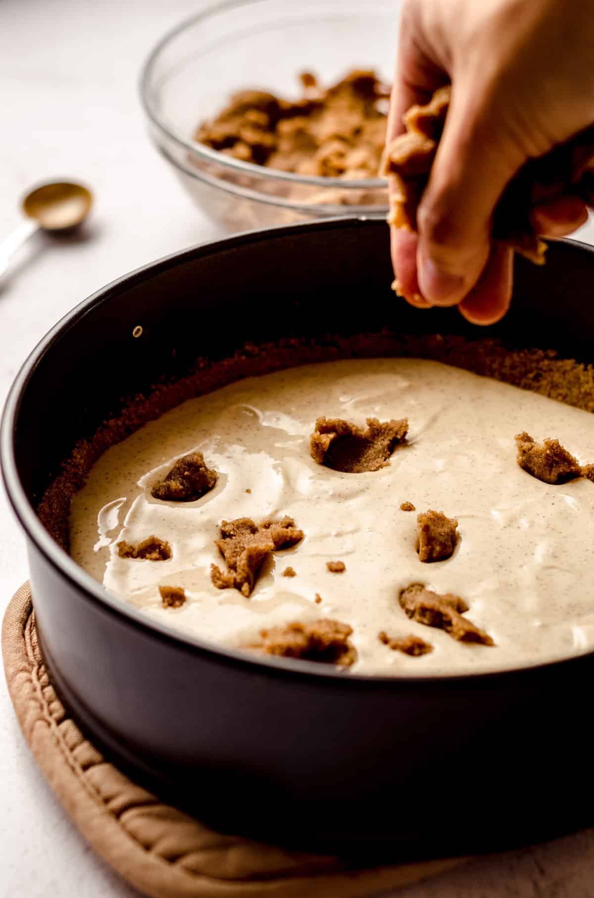 hand dropping chunks of cinnamon roll filling into cinnamon roll cheesecake batter