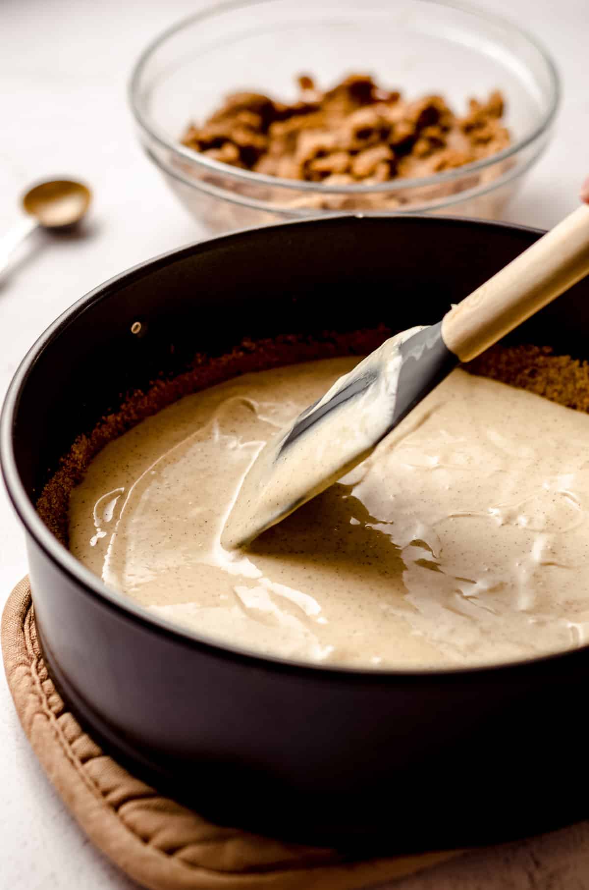 spatula spreading cinnamon roll cheesecake batter onto a nilla wafer crust