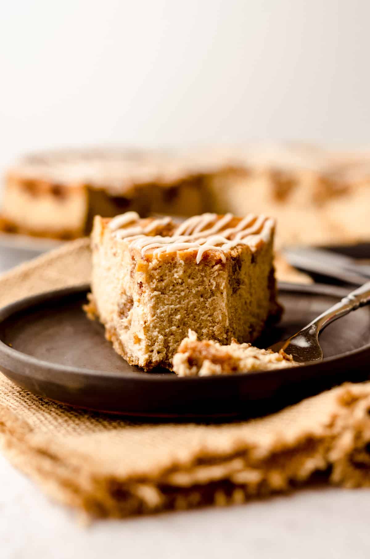 slice of cinnamon roll cheesecake on a plate with a bite taken out of it