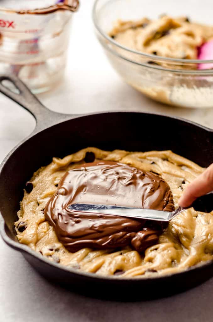spreading nutella onto chocolate chip cookie dough in a skillet