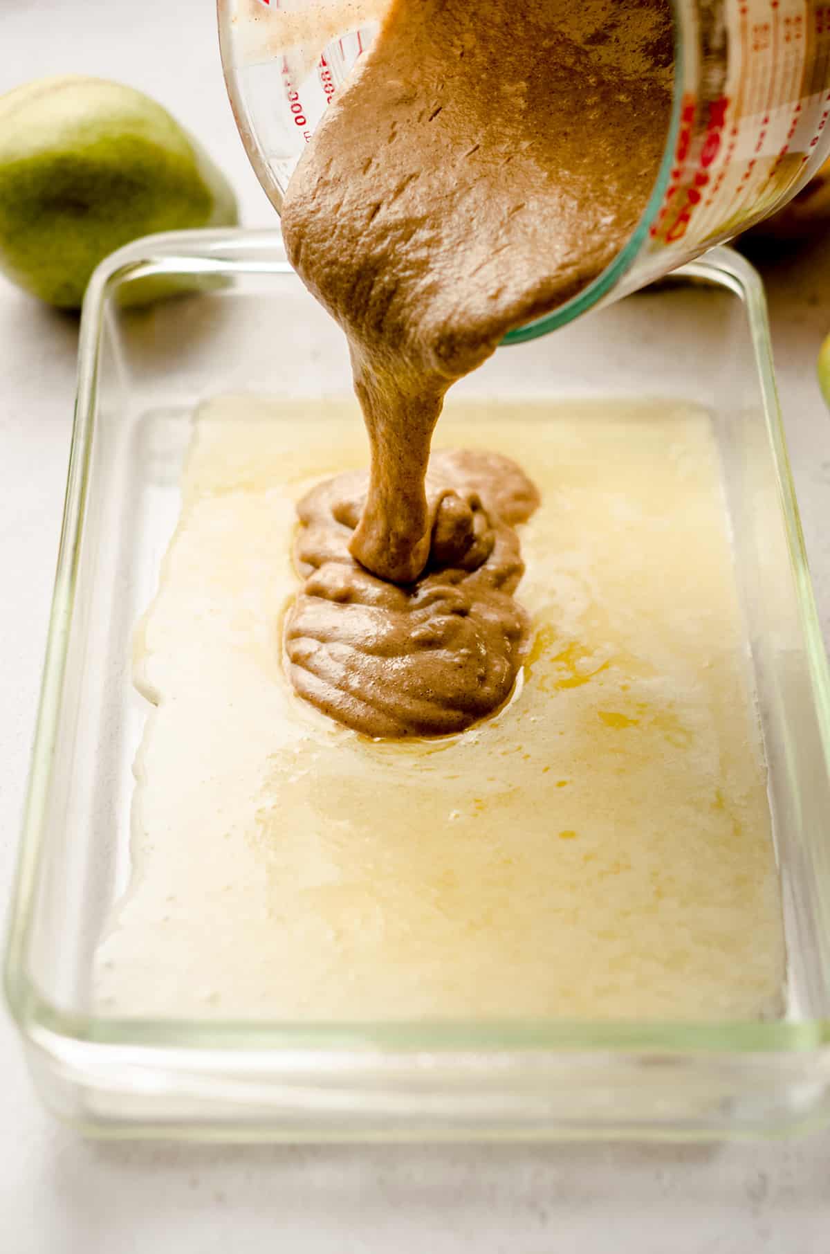 pouring biscuit batter into a baking pan for pear cobbler