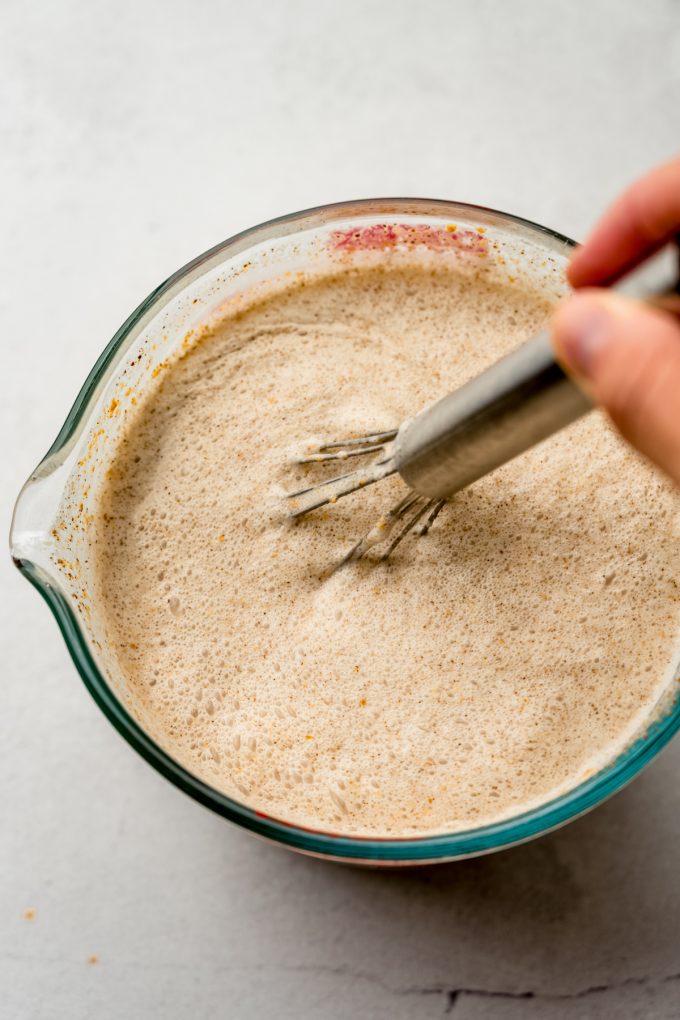 Someone is whisking a large glass measuring cup full of ingredients to make pumpkin ice cream.