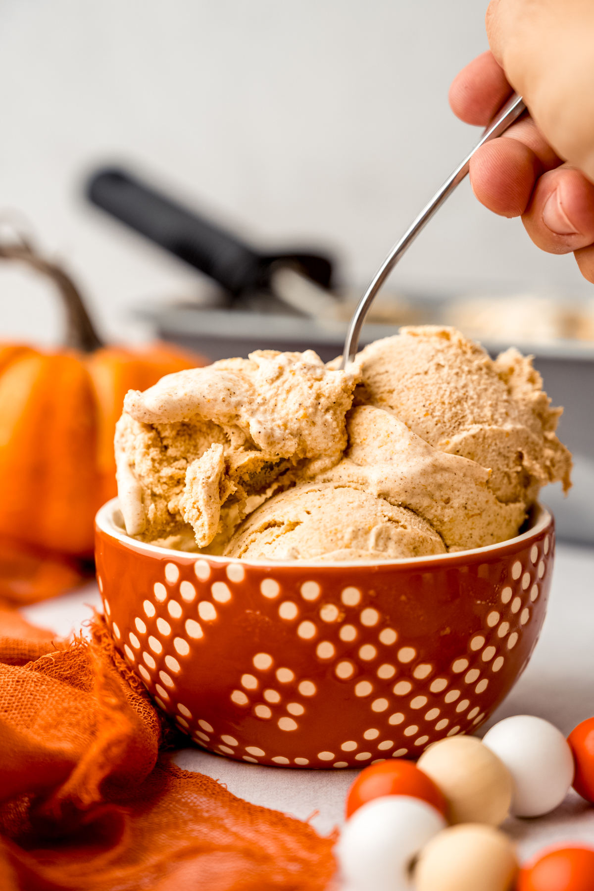 Someone is using a spoon to take a bite out of a bowl of pumpkin ice cream.