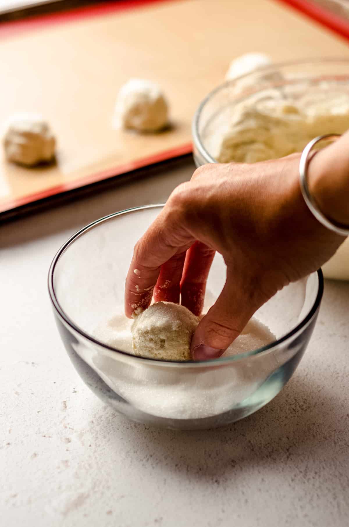 rolling vanilla bean sugar cookie dough in a bowl of sugar