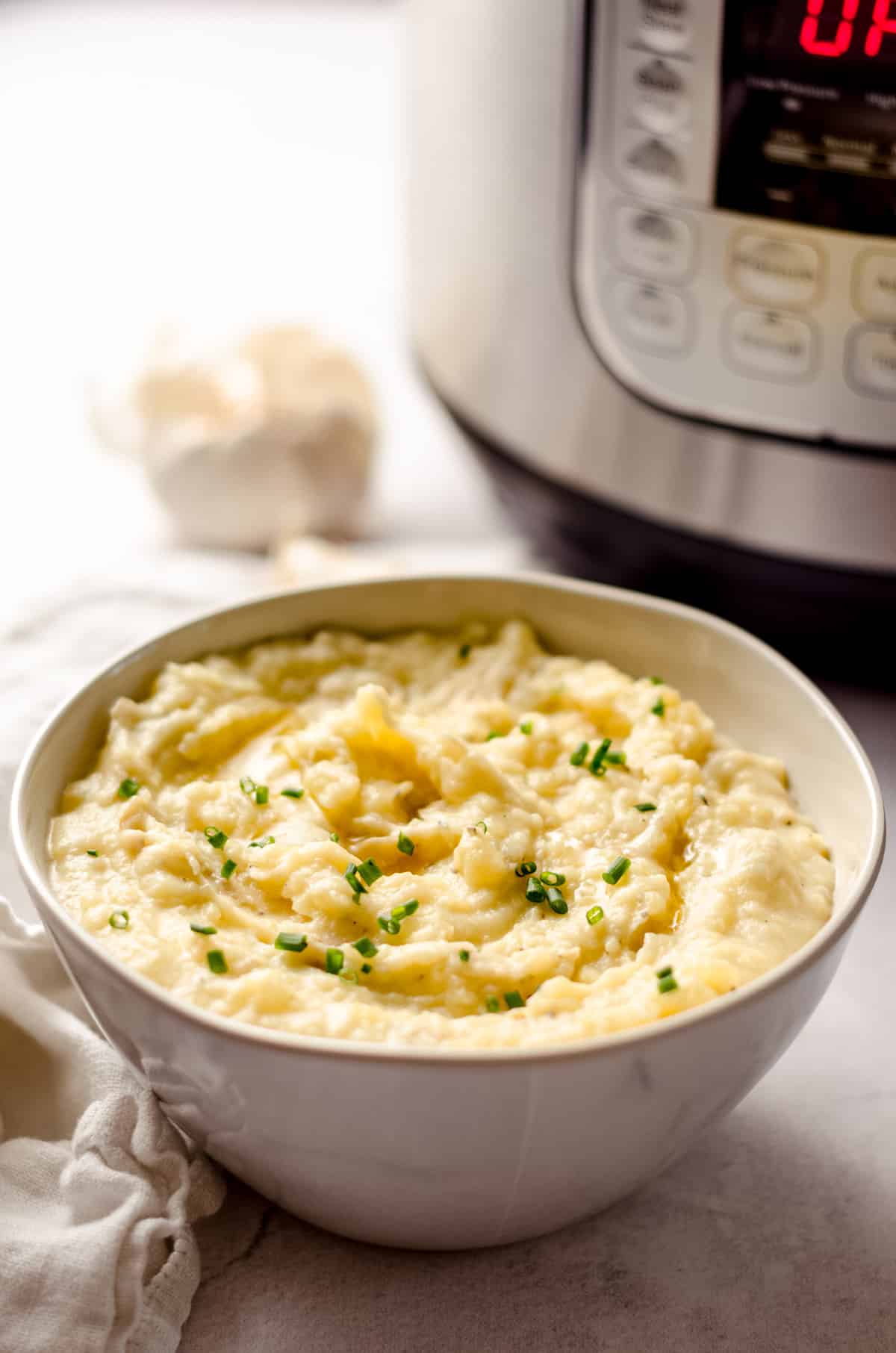 bowl of instant pot garlic mashed potatoes in front of an instant pot