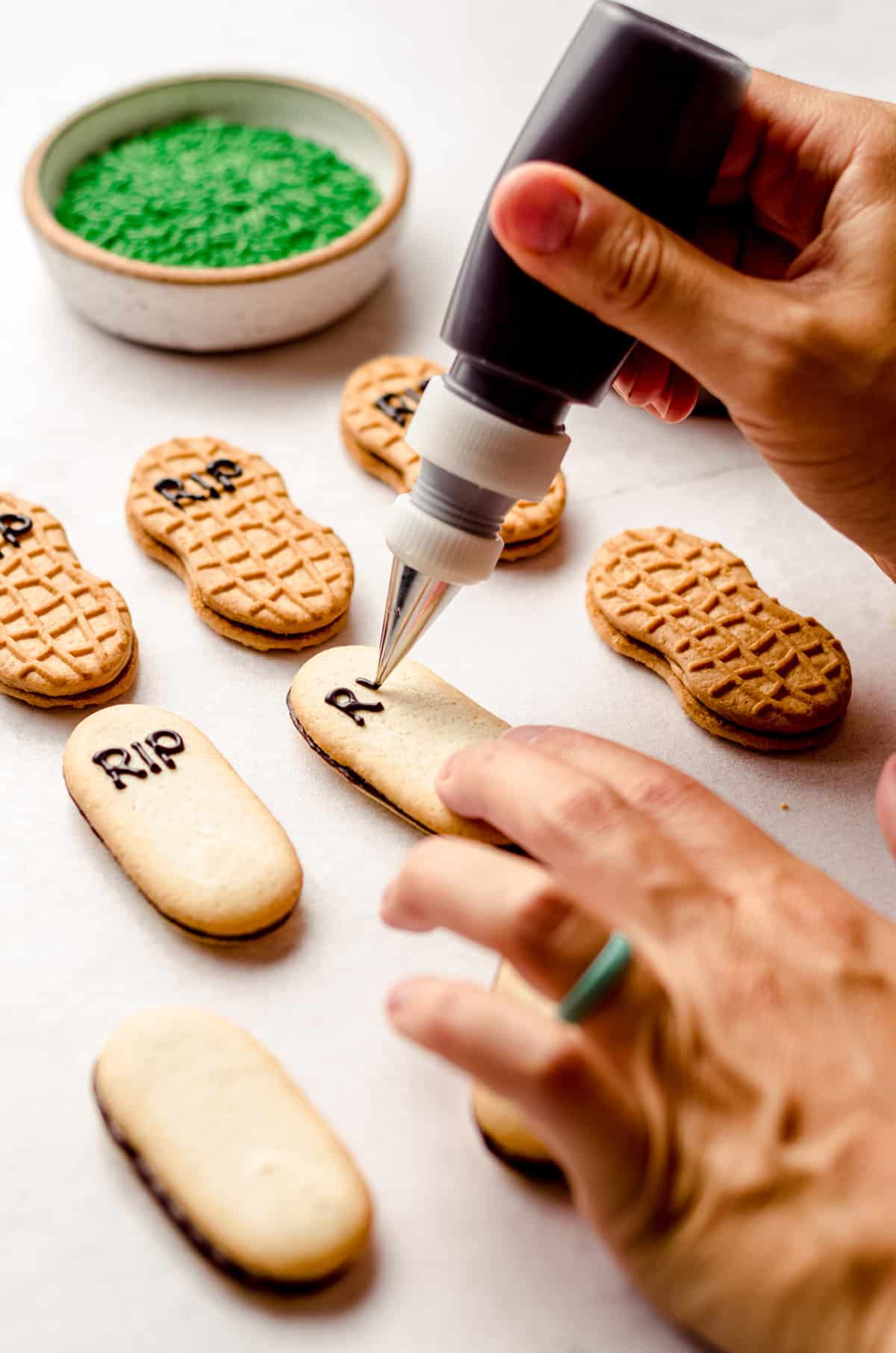 hand piping the letters R.I.P. onto a milano cookie to make a gravestone for graveyard pudding cups