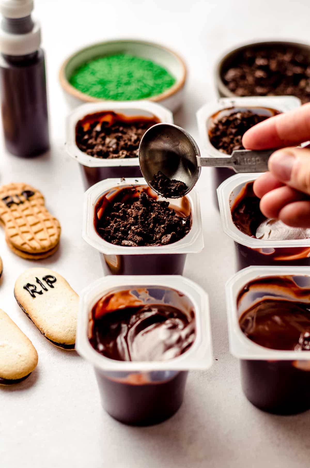 spooning crushed oreos on top of pudding cups to make graveyard dirt