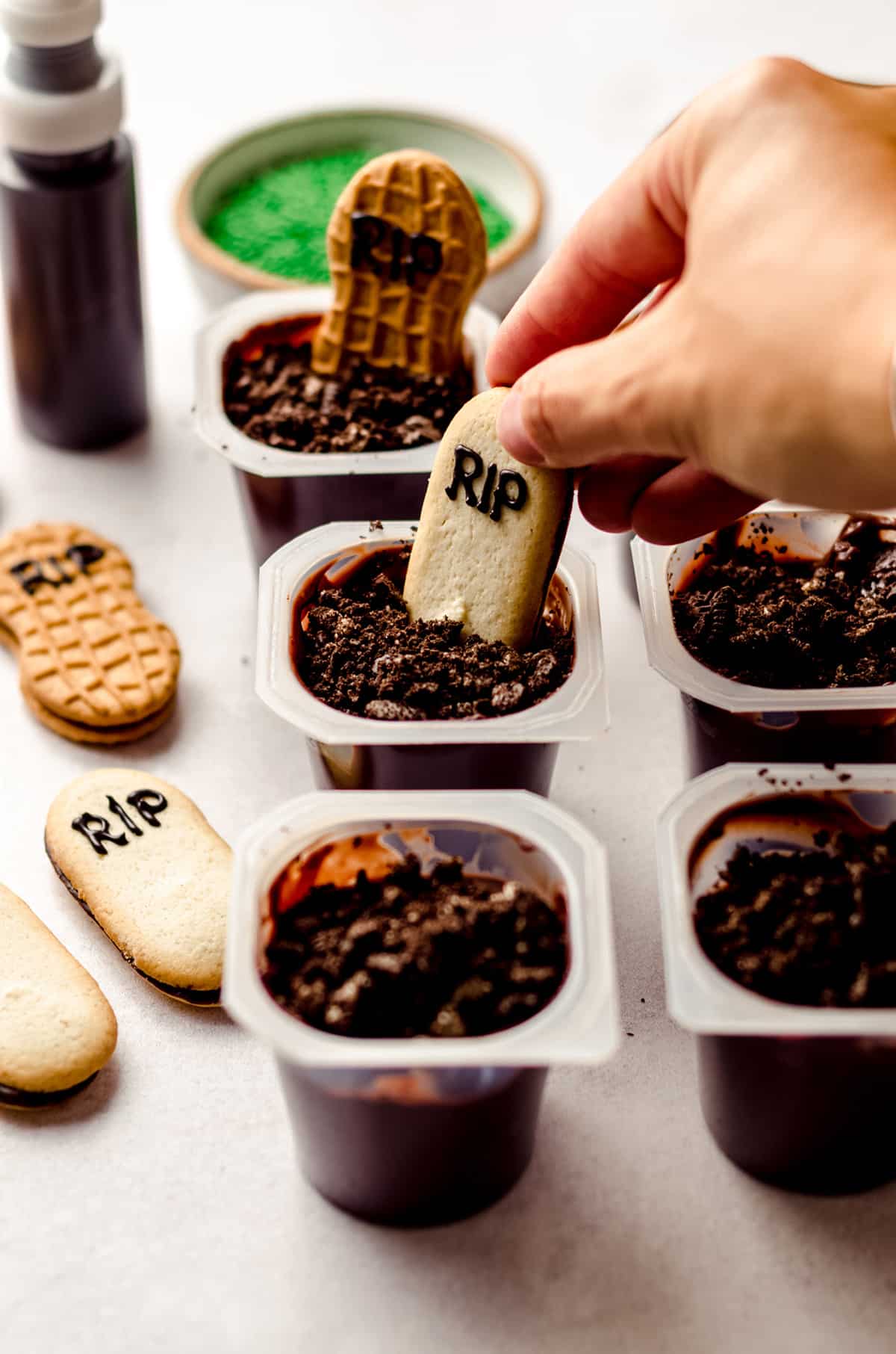 hand placing a milano cookie into a pudding cup to make graveyard pudding cup