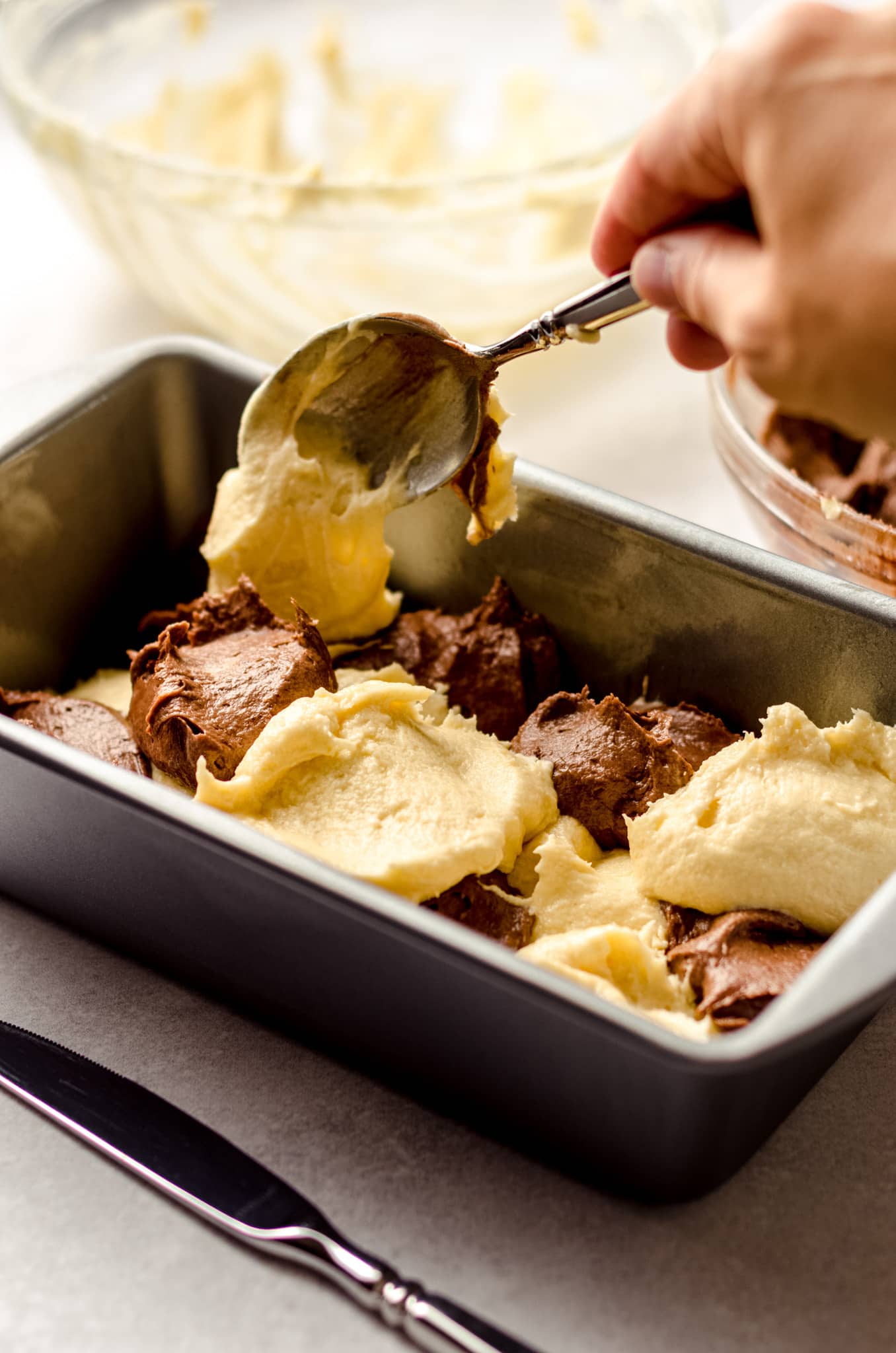 spooning batter into a loaf pan to make marble pound cake