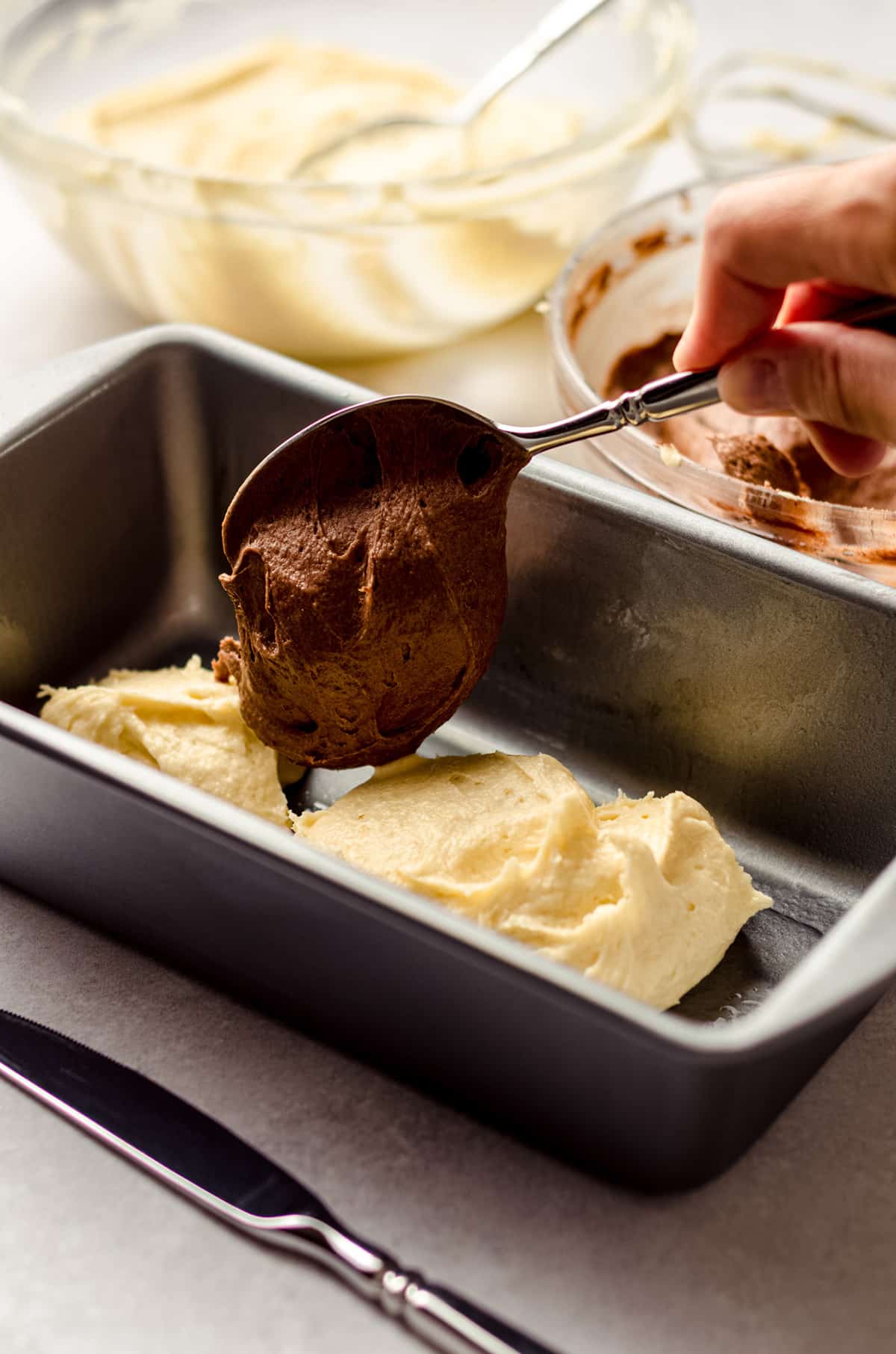 spooning chocolate batter into a loaf pan for marble pound cake