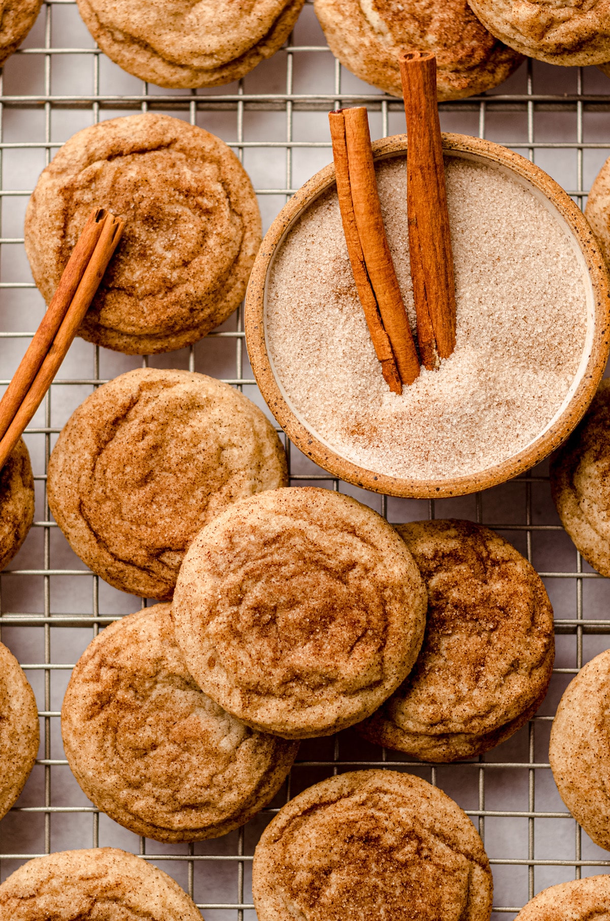 aerial photo of snickerdoodles on a cooling rack with a bowl of cinnamon sugar and cinnamon sticks