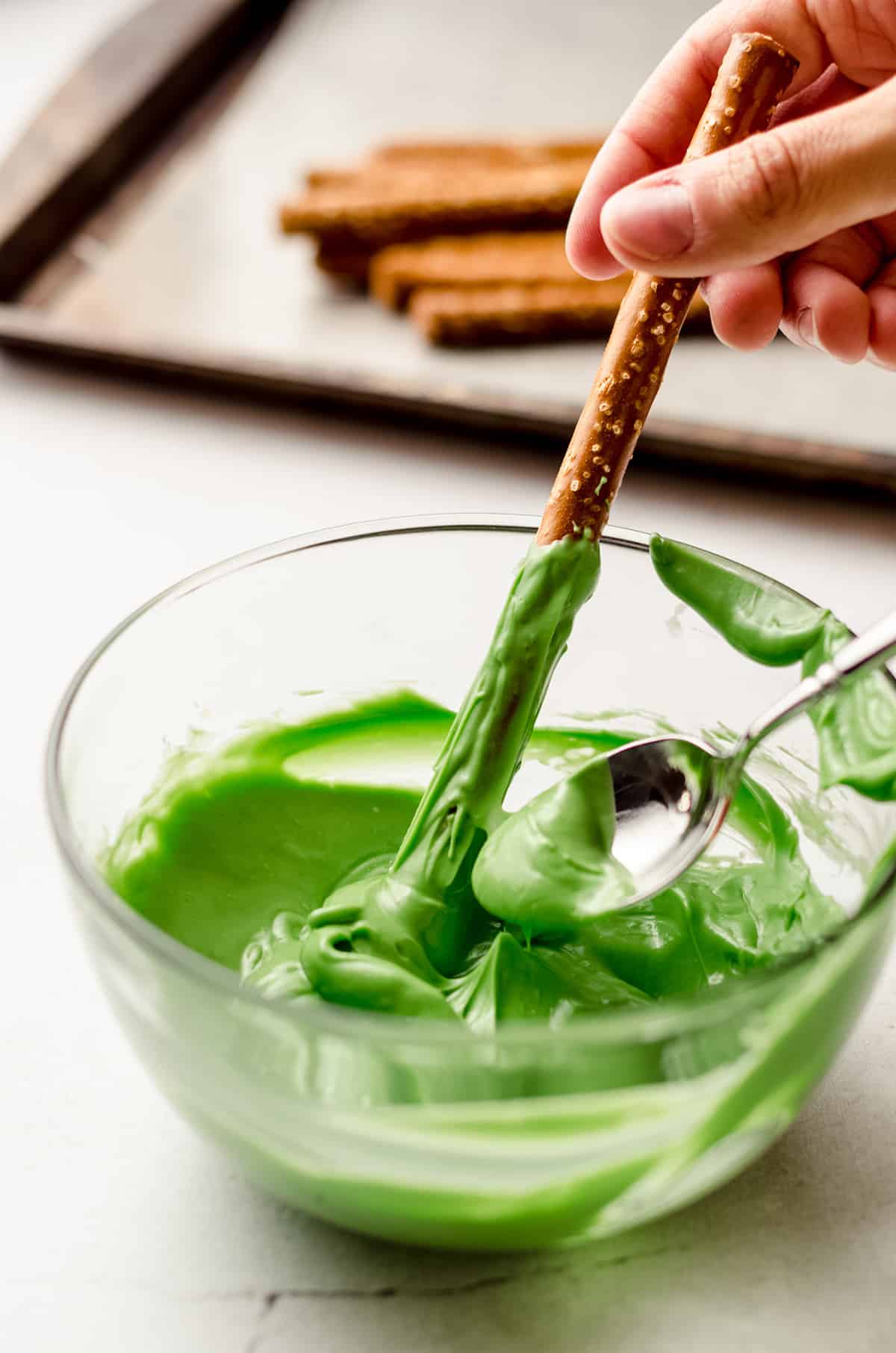 dipping a pretzel rod into green candy coating to make witch finger pretzels