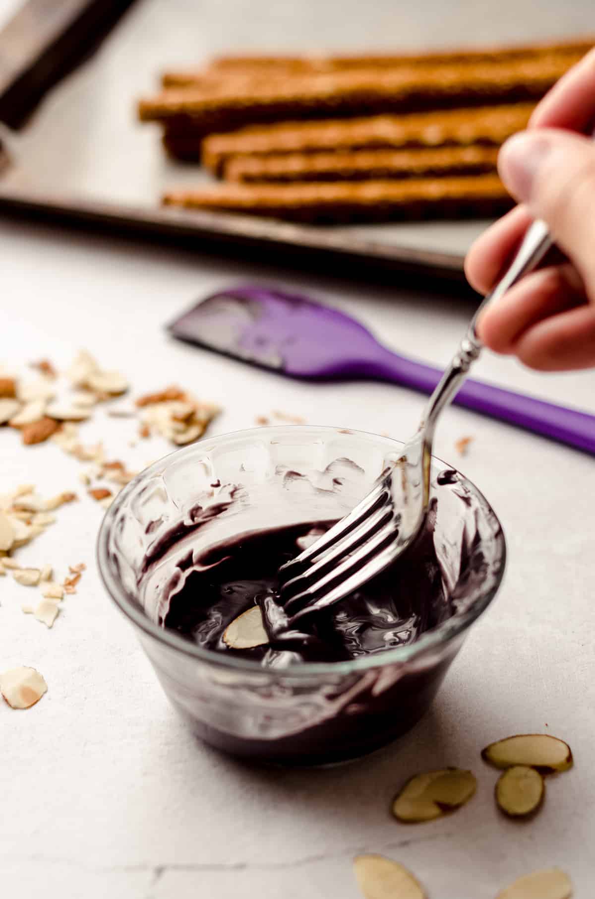 dipping slivered almonds into black candy melts to make nails on witch finger pretzels