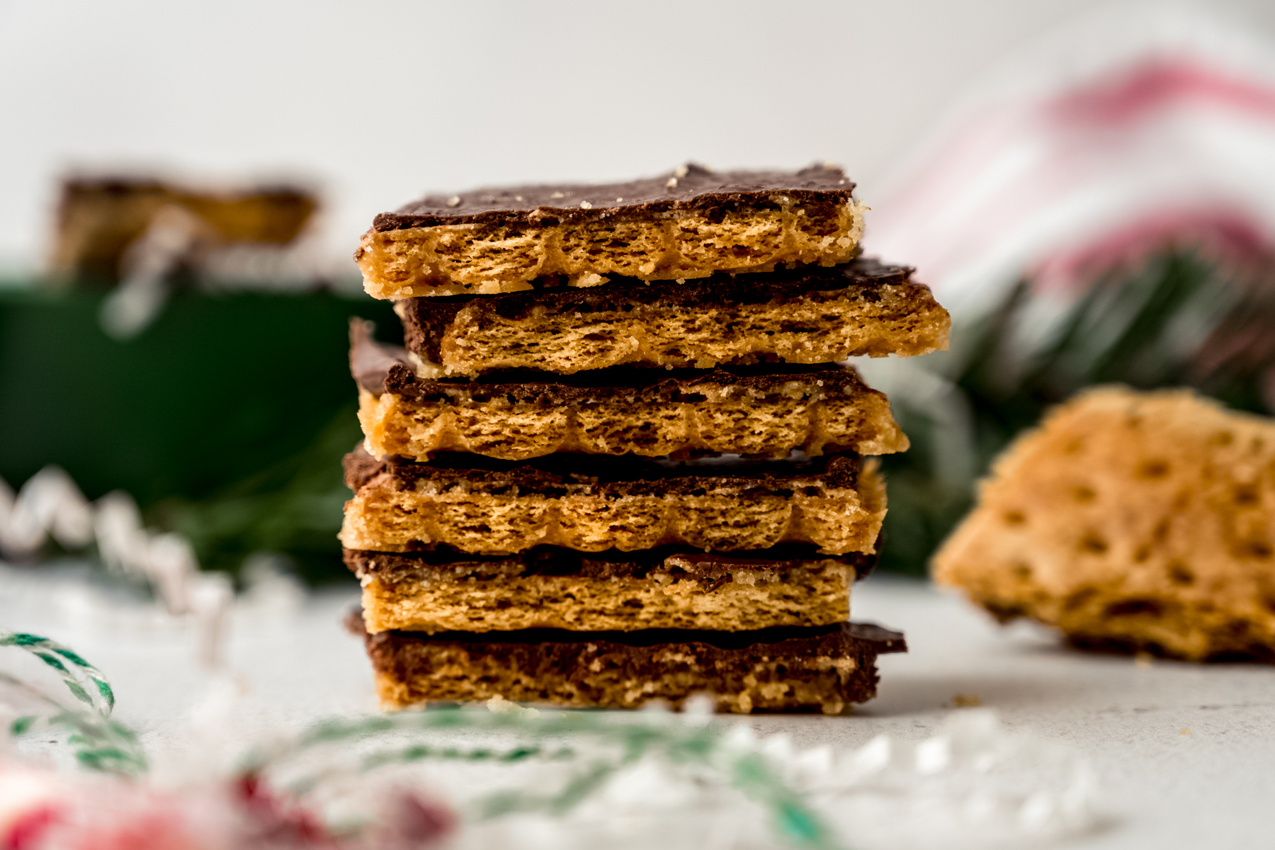 A stack of piece of graham cracker toffee bark on a surface with Christmas decor around it.