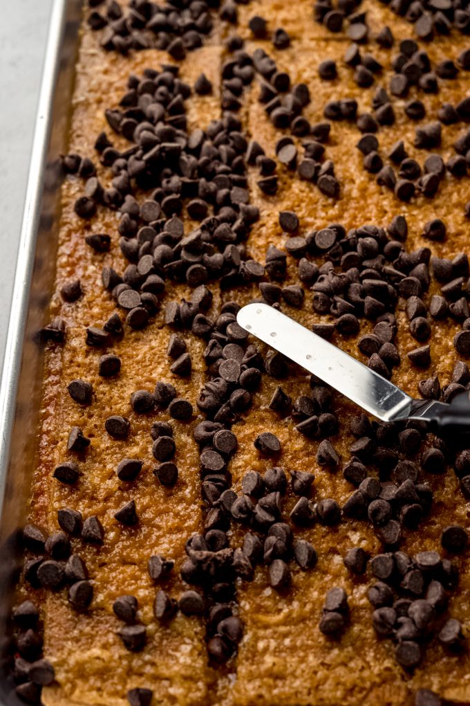 Someone is using a metal offset spatula to spread melting chocolate chips onto the surface of toffee bark.