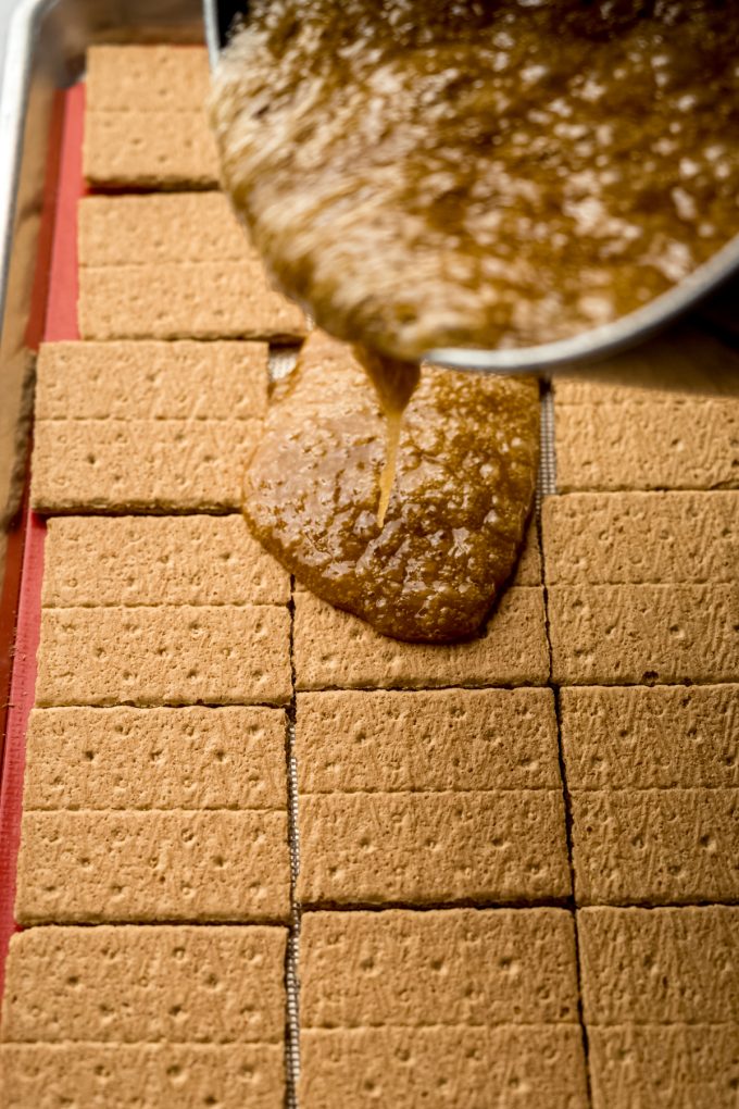 Someone is pouring toffee mixture onto graham crackers to make toffee bark.