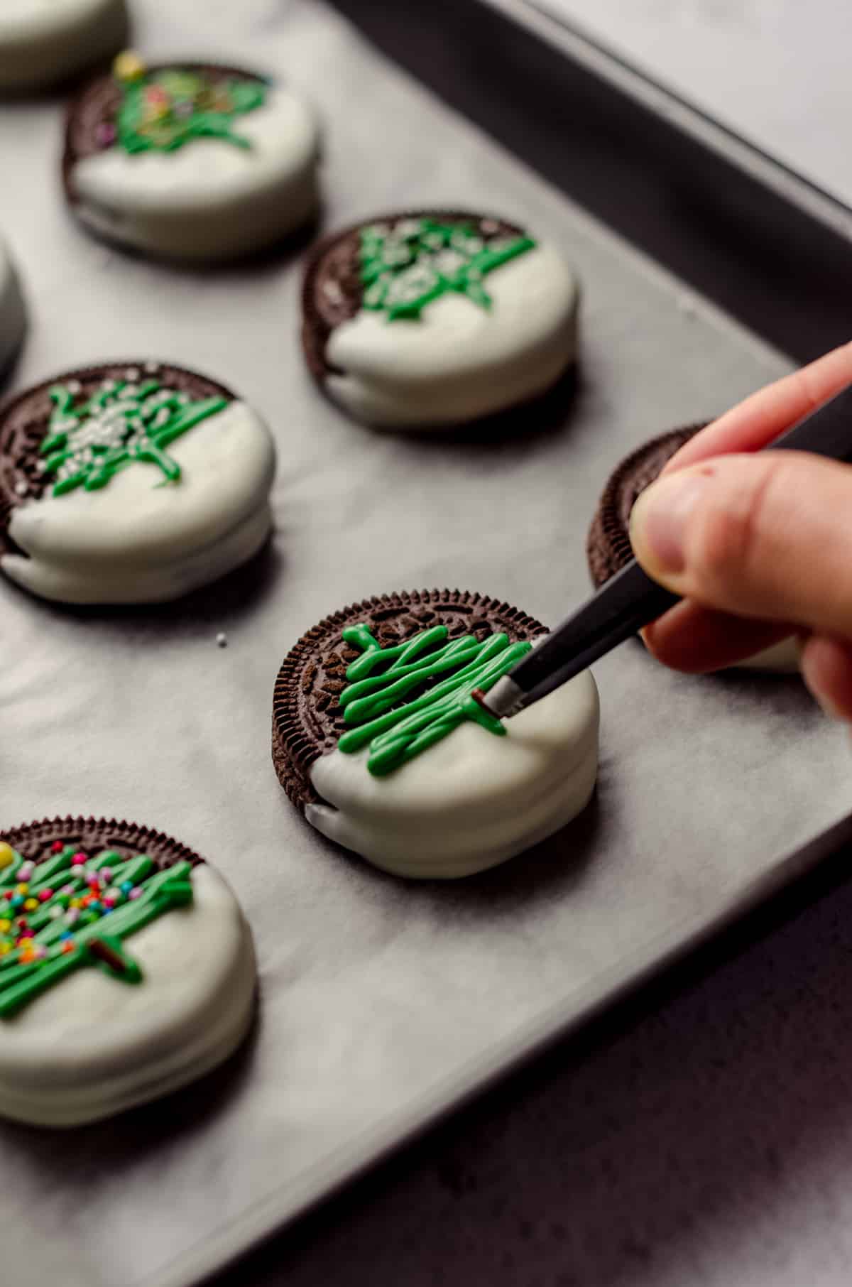 tweezers placing a chocolate jimmie onto a green christmas tree piped onto a white chocolate dipped oreo
