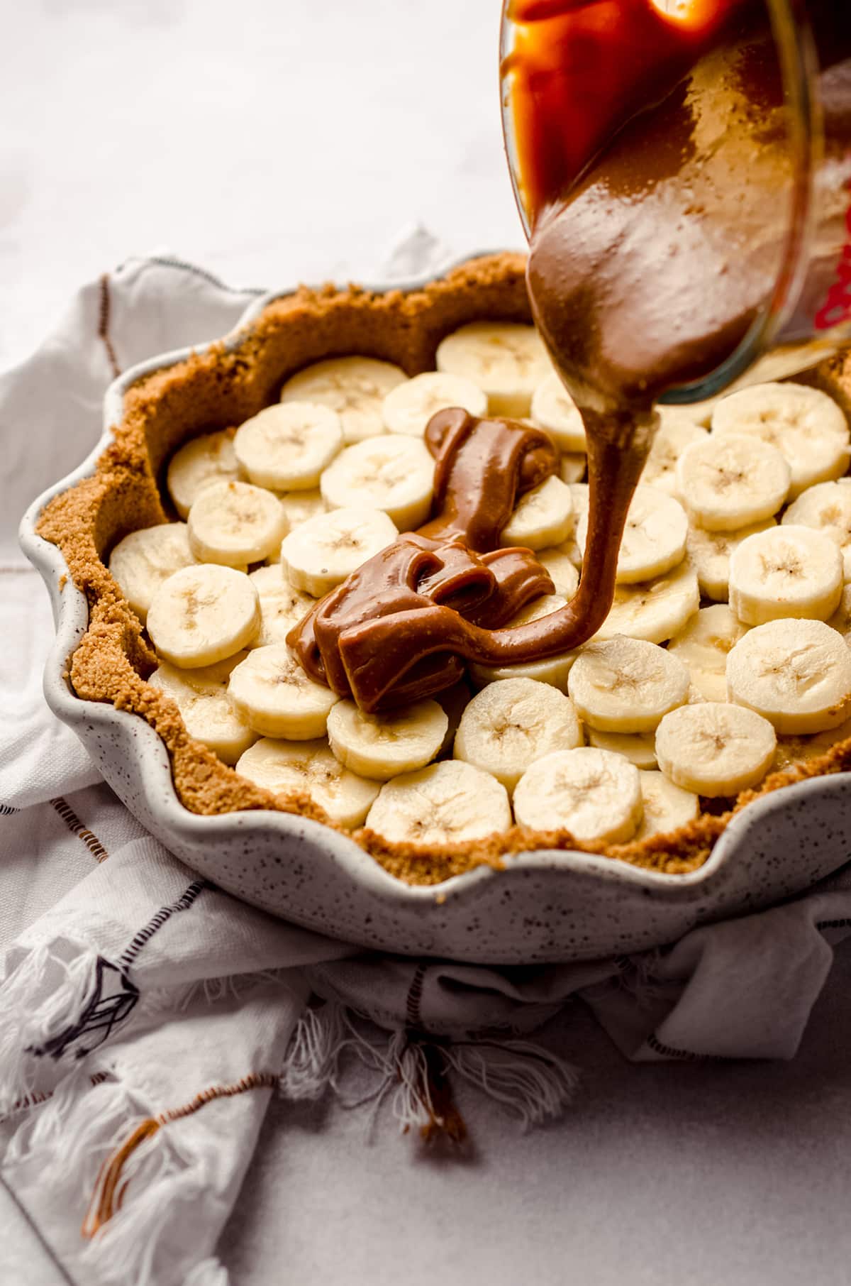 pouring dulce de leche onto banana layer in banoffee pie