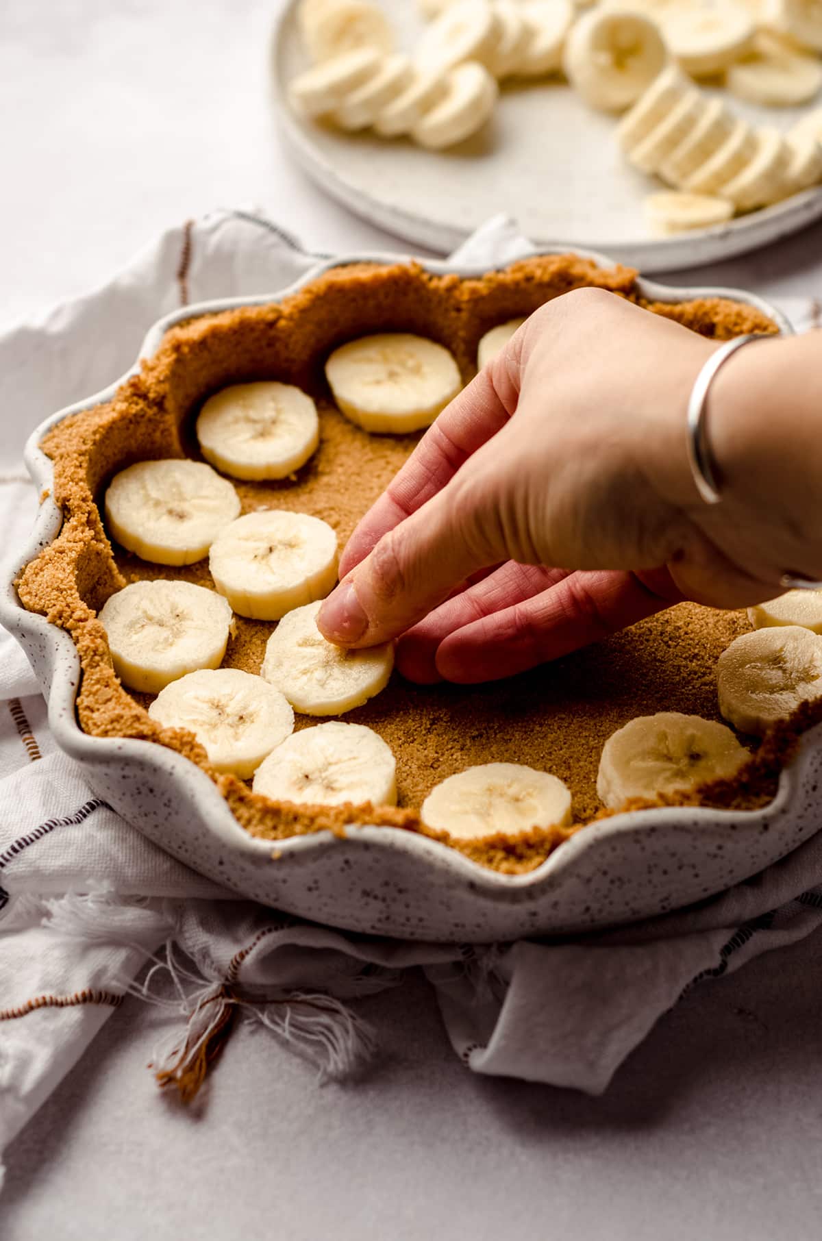 placing bananas into a graham cracker crust for banoffee pie