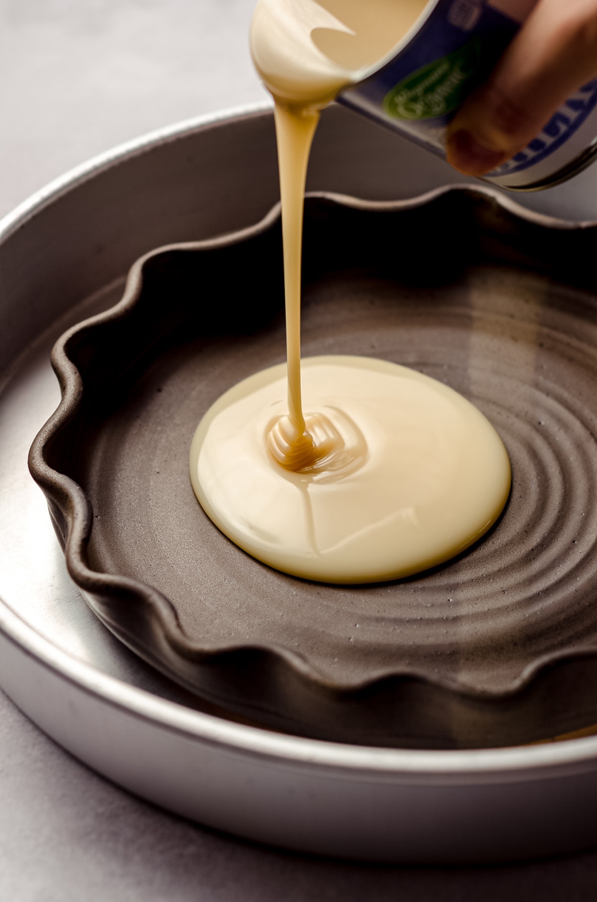 pouring sweetened condensed milk into a pie plate to make dulce de leche