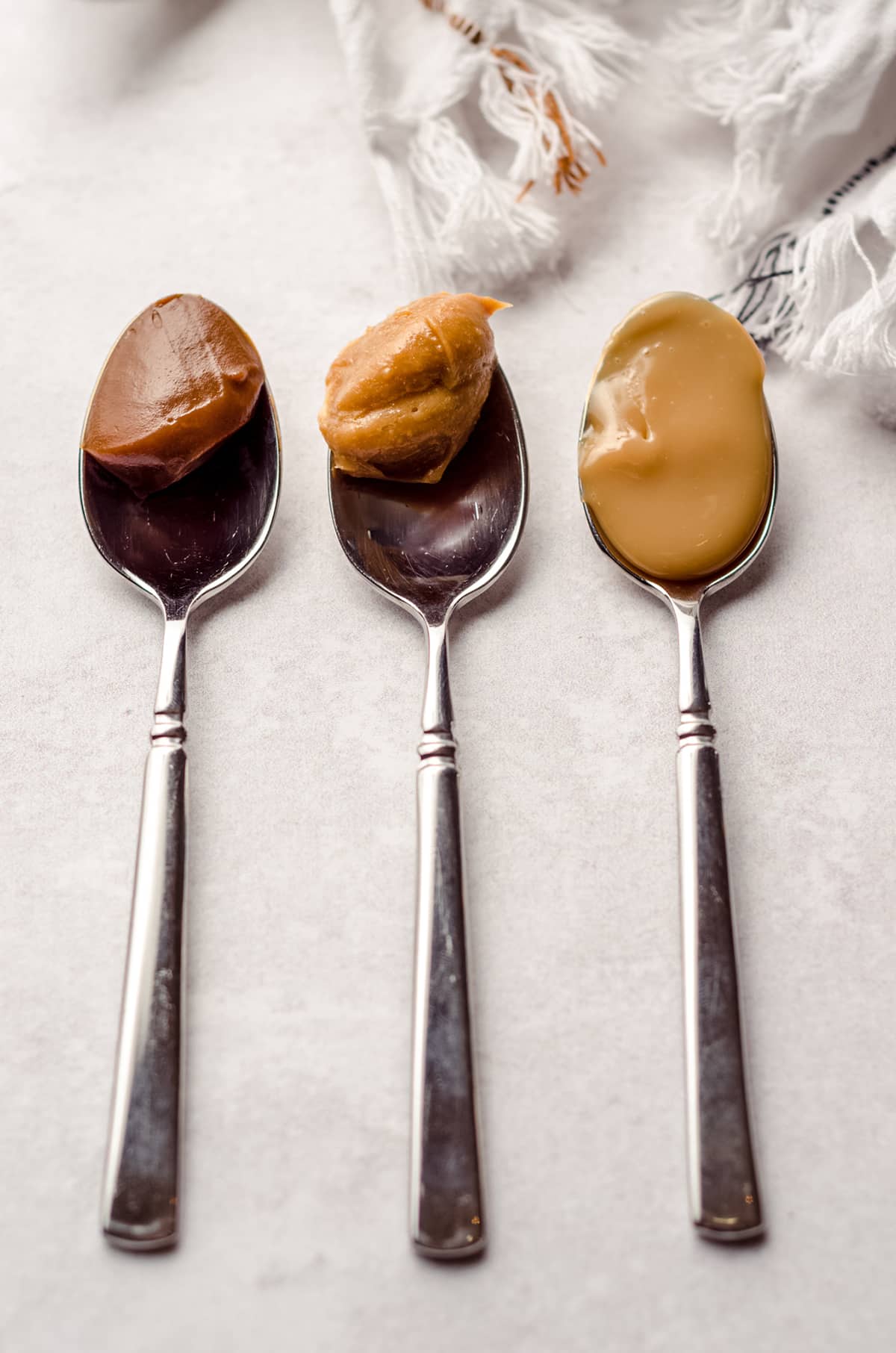 three spoons with store bought, baked, and boiled homemade dulce de leche on them to show differences