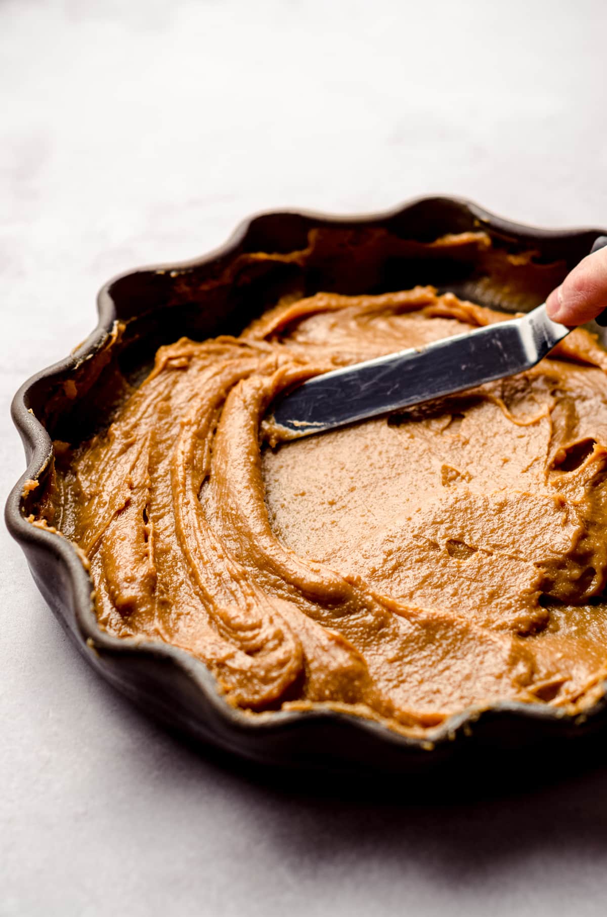 spreading warm homemade dulce de leche in a pie plate with a spatula