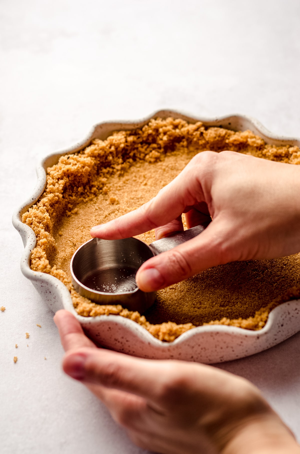 using a measuring cup to press graham cracker crust into a pie plate