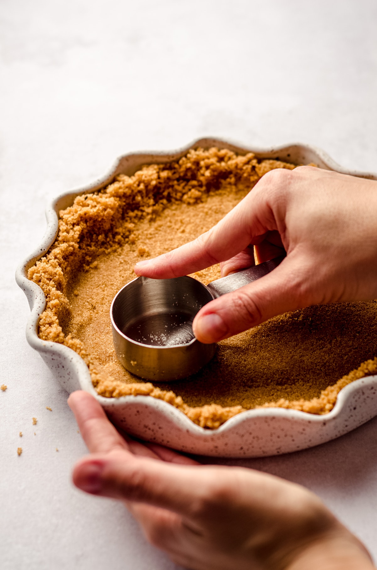 using a measuring cup to press graham cracker crust into a pie plate