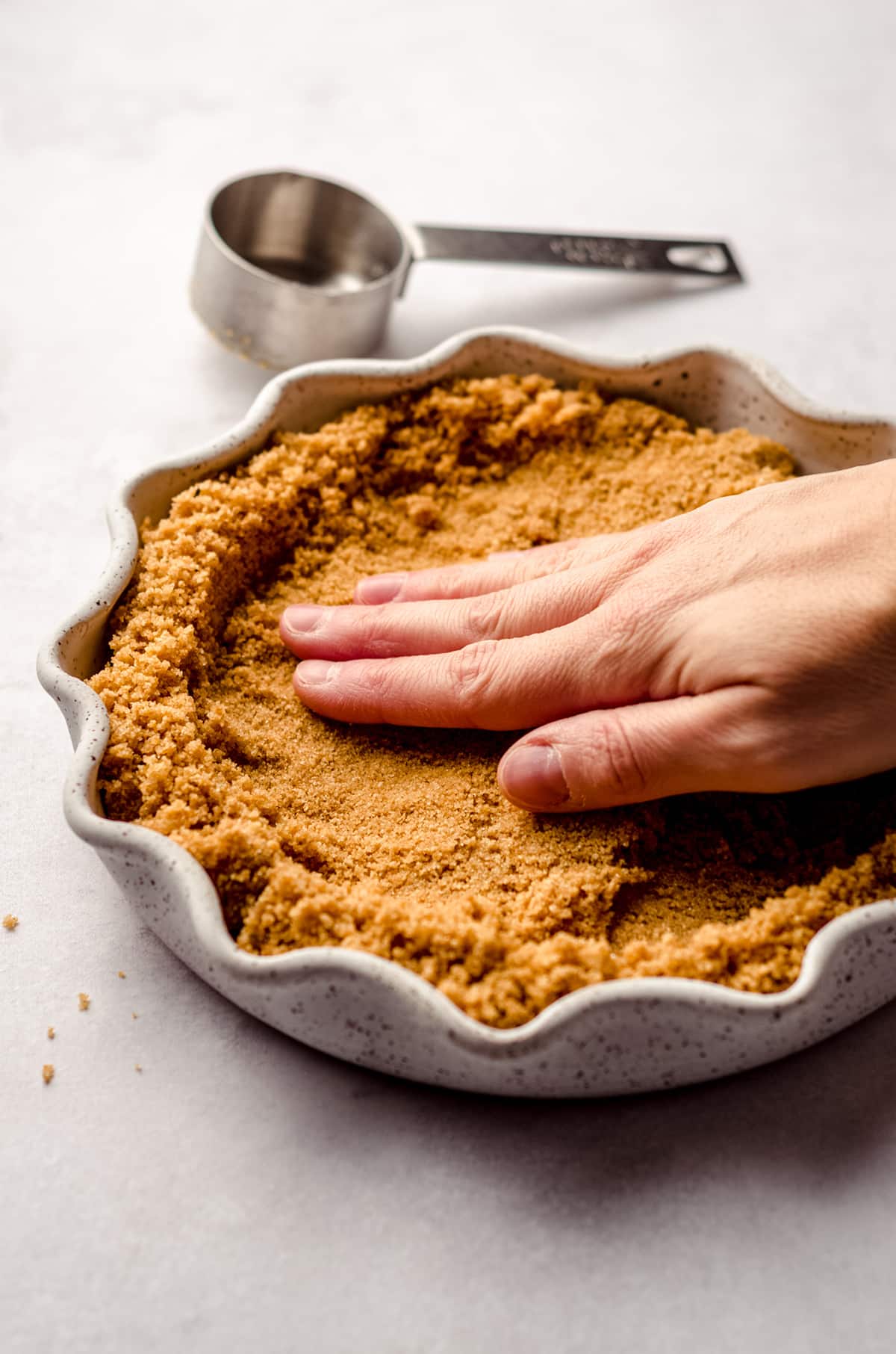 hand pressing a graham cracker crust into a pie plate