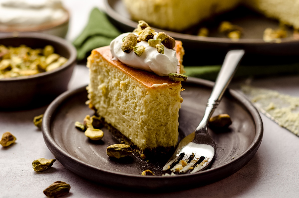 slice of pistachio cheesecake on a plate with a bite taken out of it