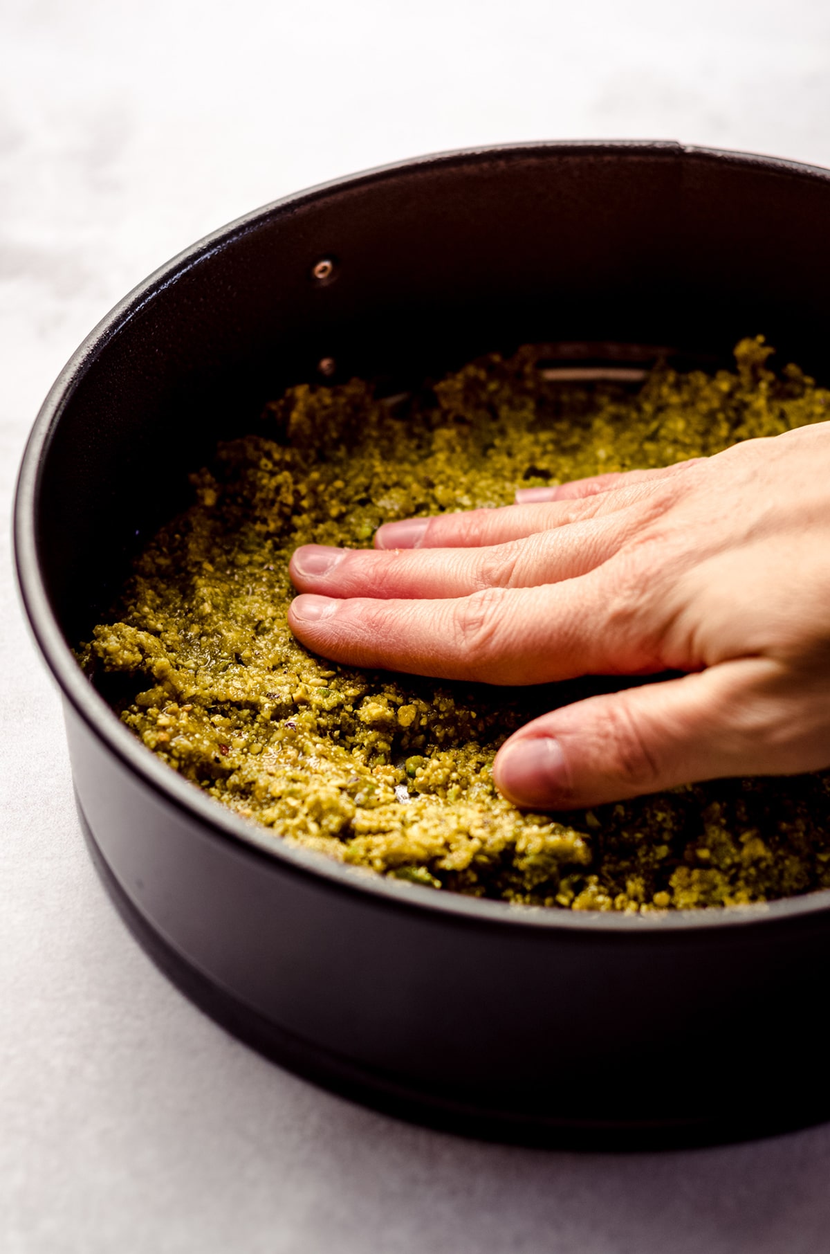 hand pressing a pistachio crust into the bottom of a springform pan