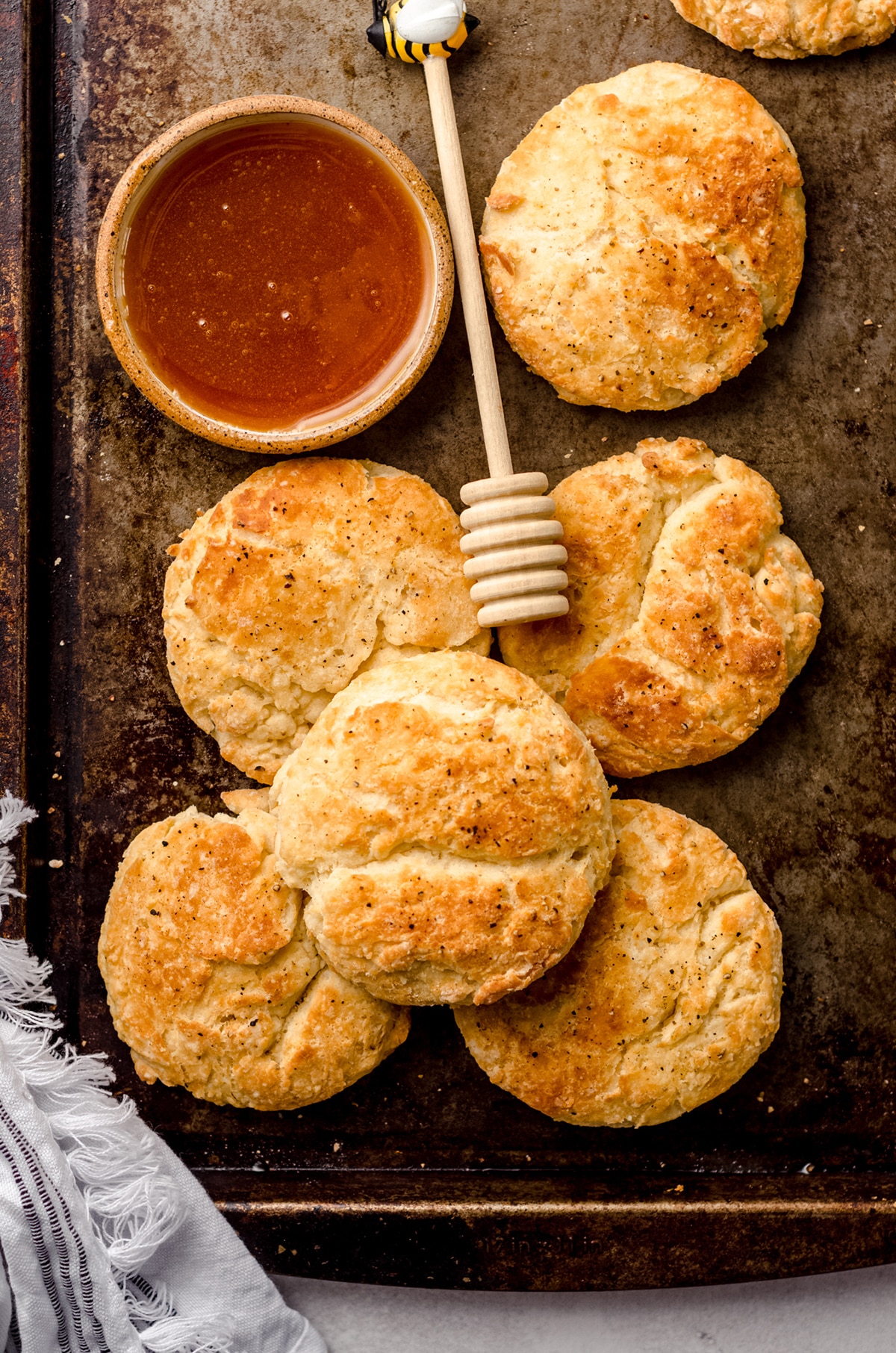 aerial photo of buttermilk biscuits on a baking sheet with a bowl of honey and a honey dipper