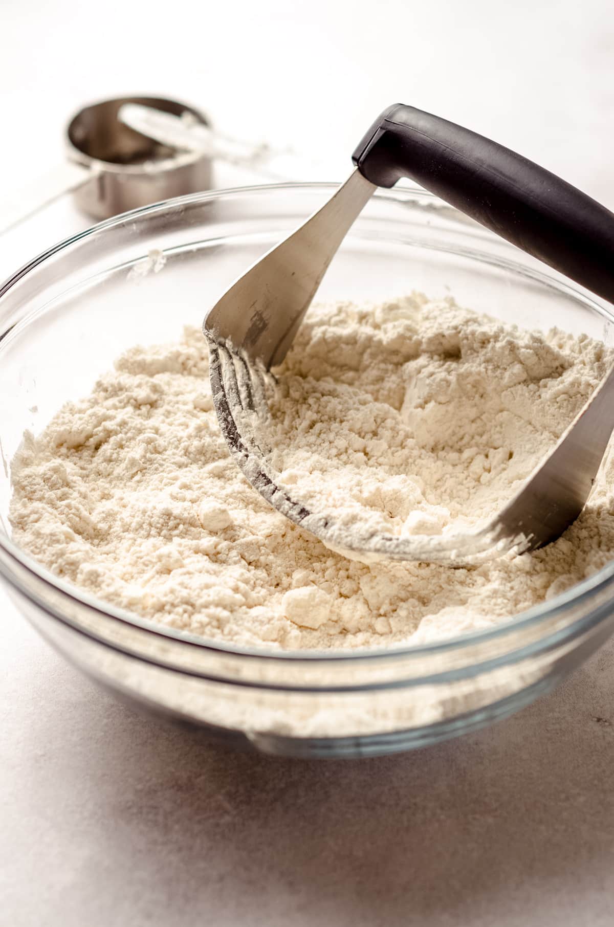 a pastry cutter in a bowl of ingredients to make biscuits