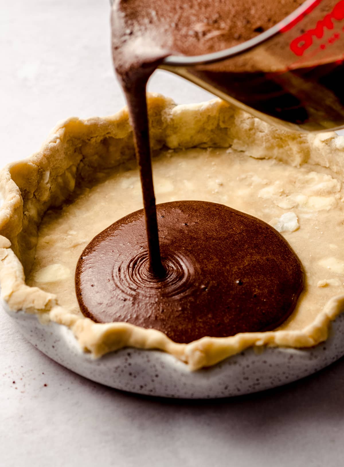 pouring chocolate chess pie filling into an unbaked pie plate