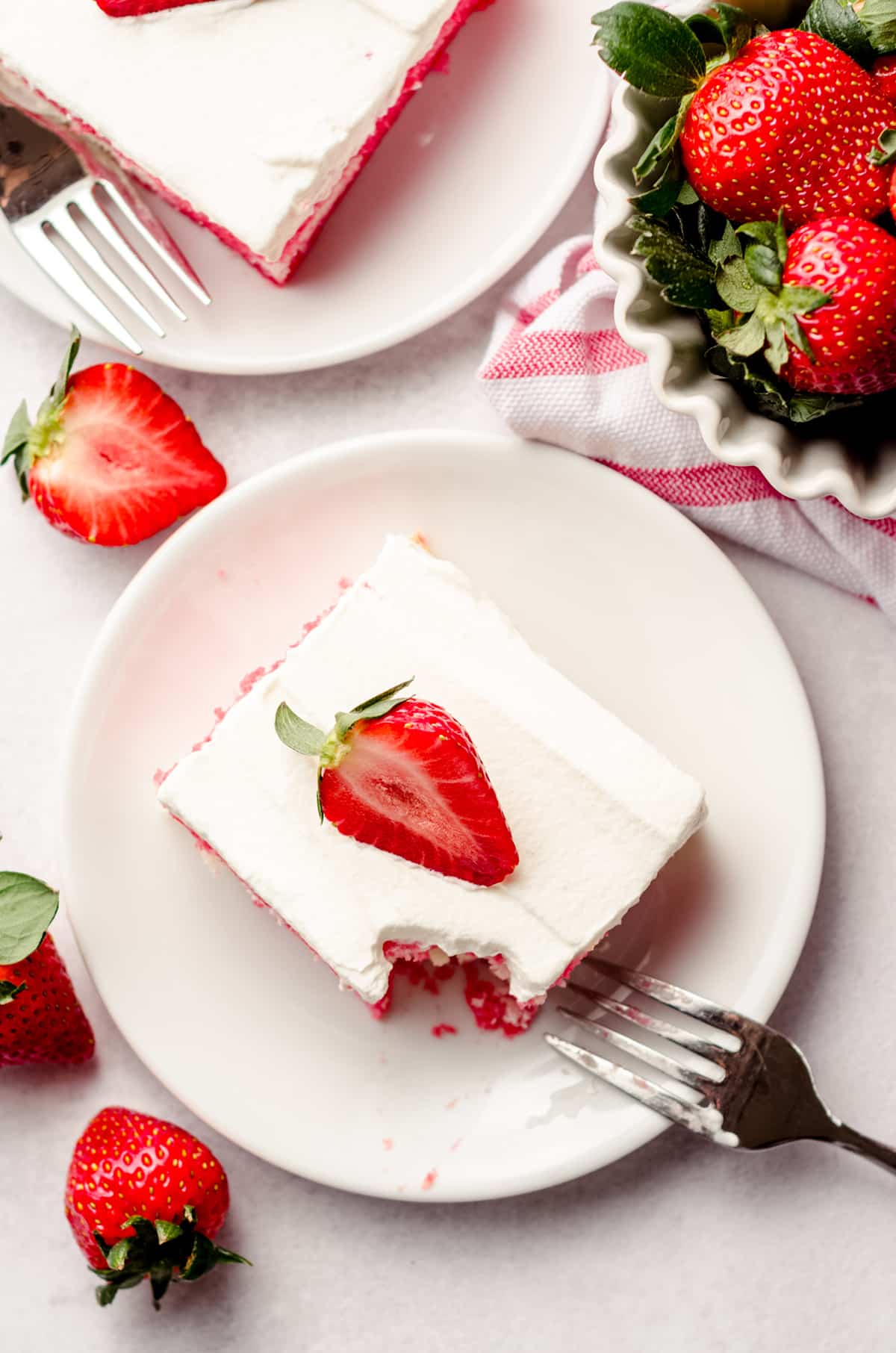 aerial photo of slice of strawberry poke cake on a plate with a bite taken out of it with a fork