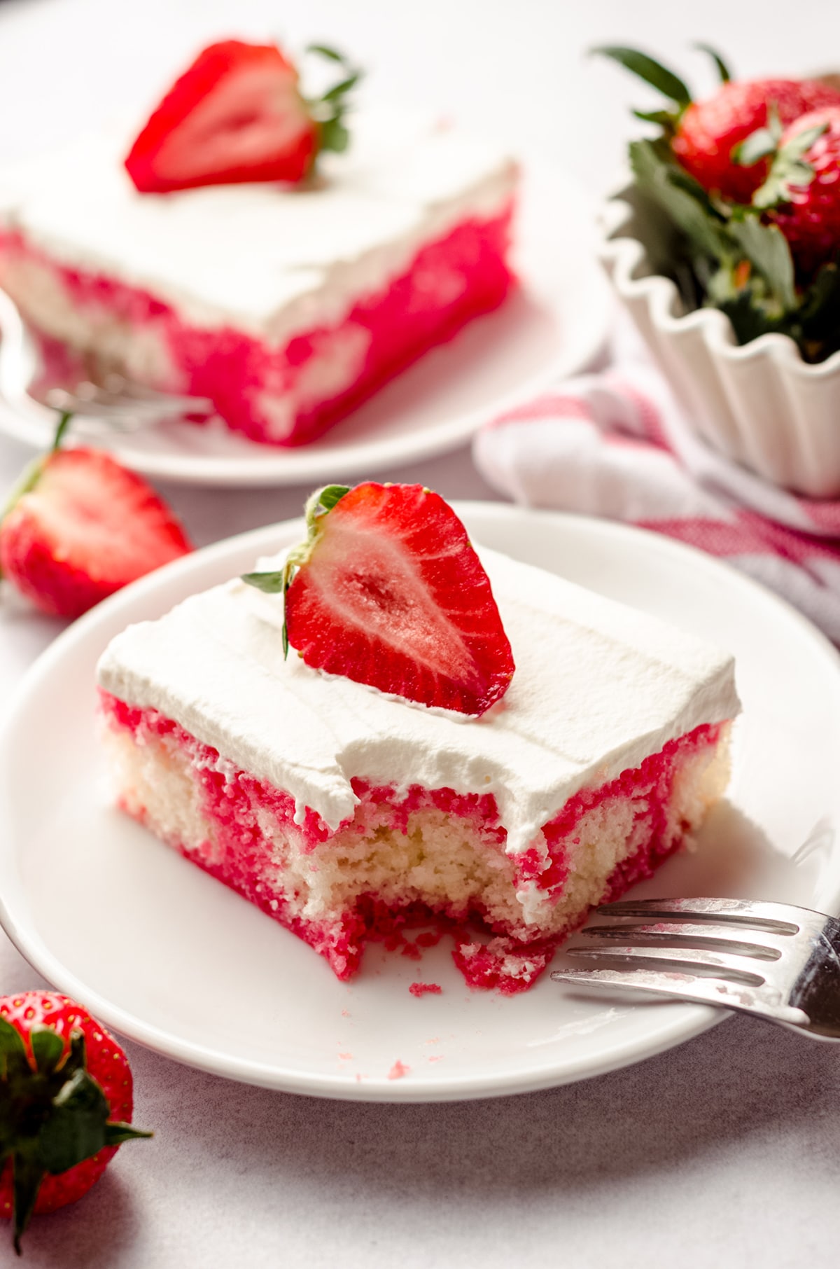 slice of strawberry poke cake on a plate with a bite taken out of it with a fork