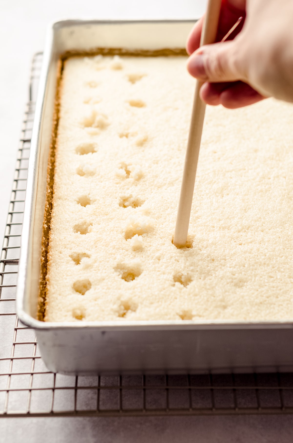 poking holes in a sheet cake to make strawberry poke cake