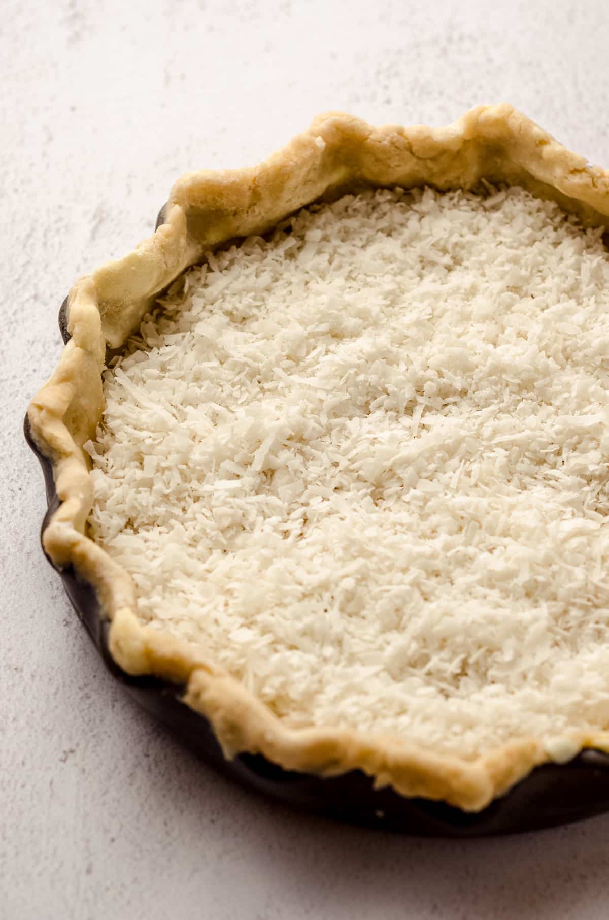 A pie crust in a pie dish, with a layer of shredded coconut at the bottom.