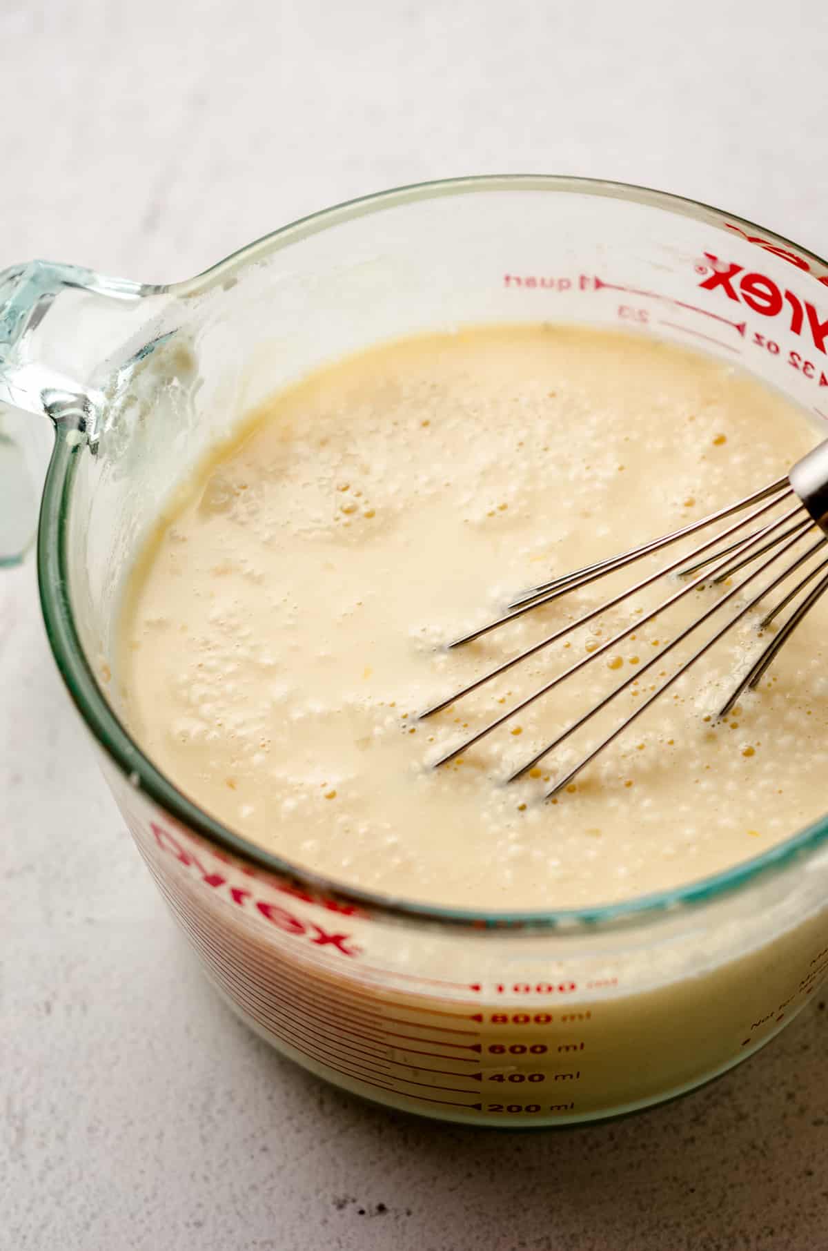 A mixing bowl, full of a liquid mixture and being whisked.