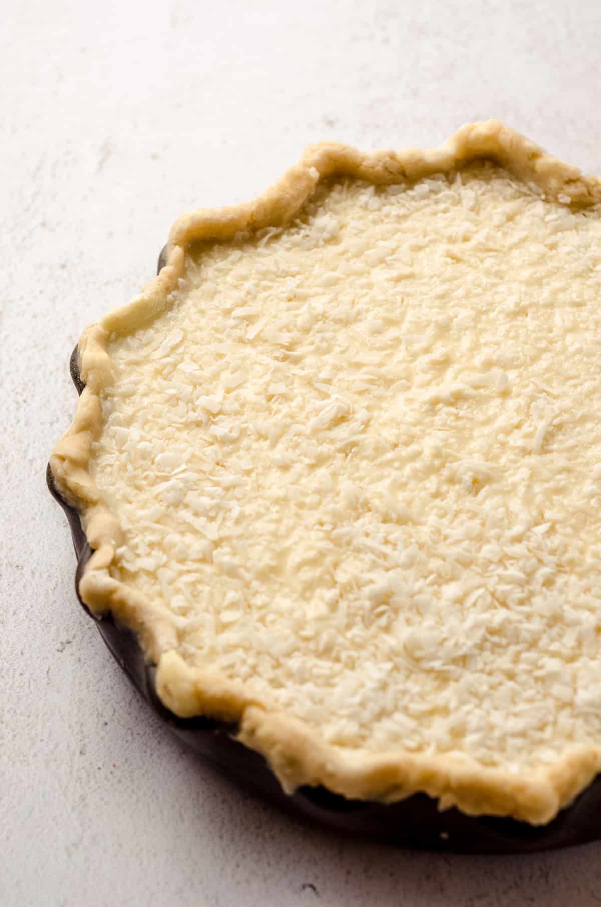 A pie crust shell filled with an unbaked custard mixture, as well as shredded coconut.