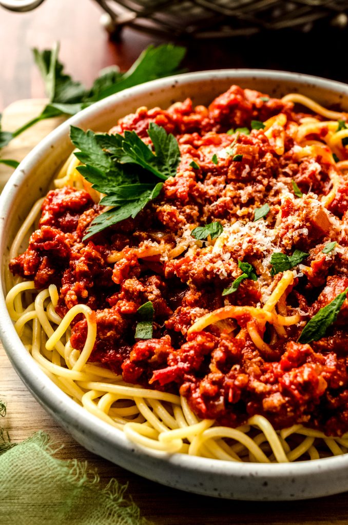 A bowl of spaghetti with meat sauce garnished with parsley and grated cheese.