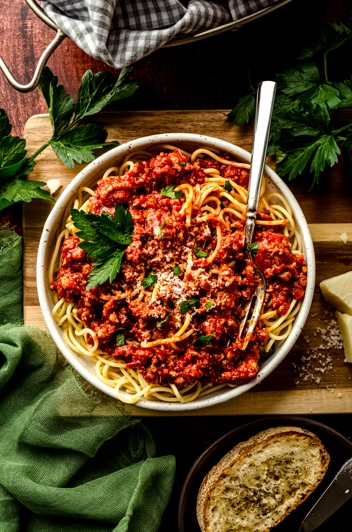 Aerial photo of a bowl of pasta with homemade meat sauce on it. There is a fork in the bowl and the plate is garnished with parsley and grated cheese.