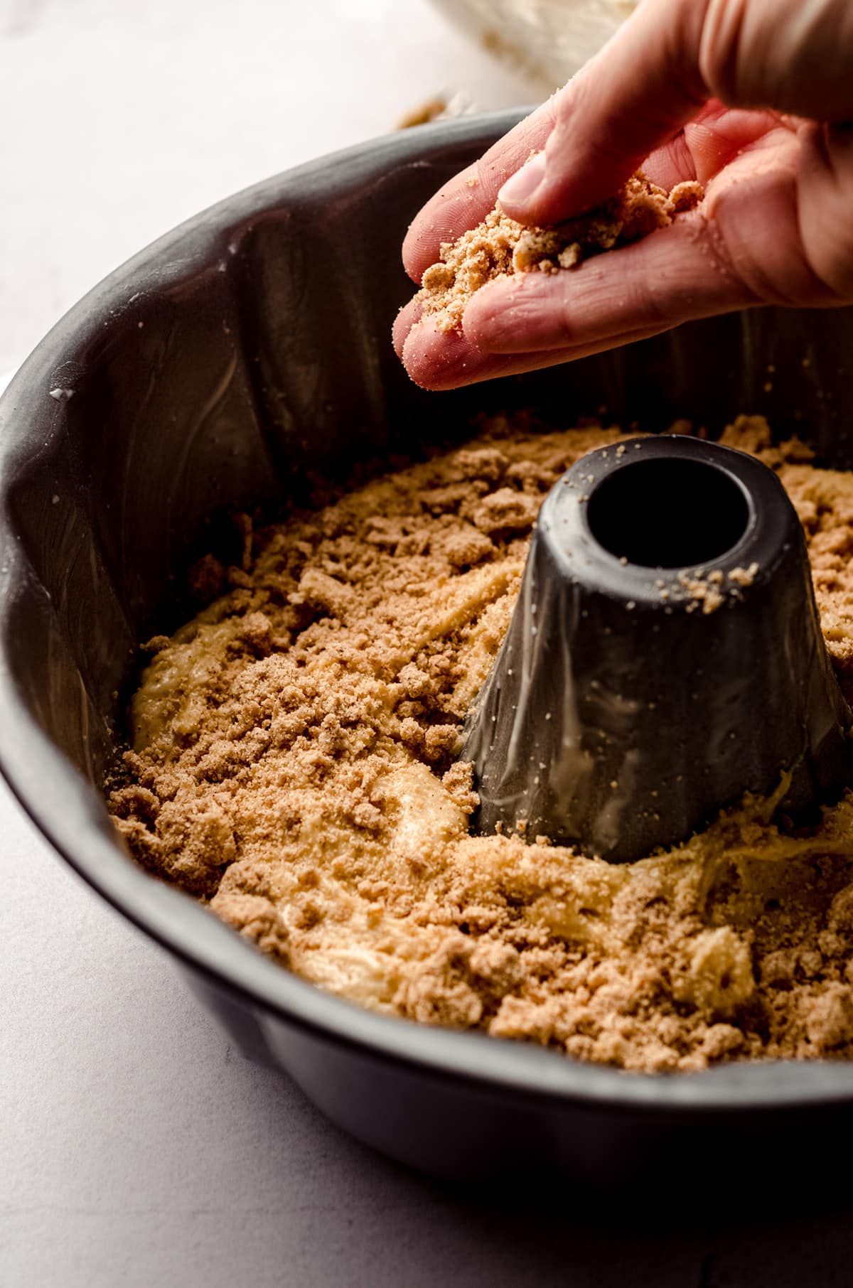 hand dropping homemade streusel topping onto coffee cake batter to make a streusel layer in the middle